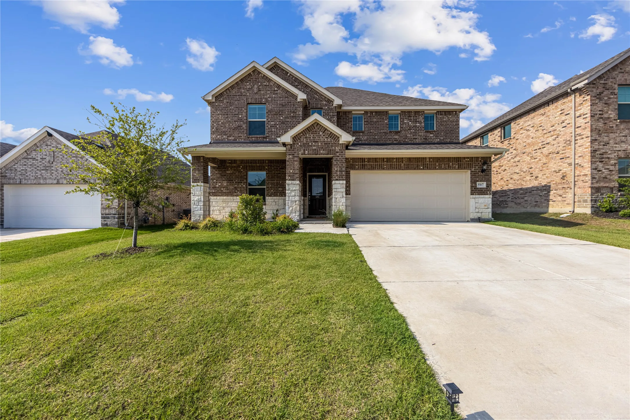 Brick and stone facade, two-car garage, concrete driveway, established lawn, and landscaping