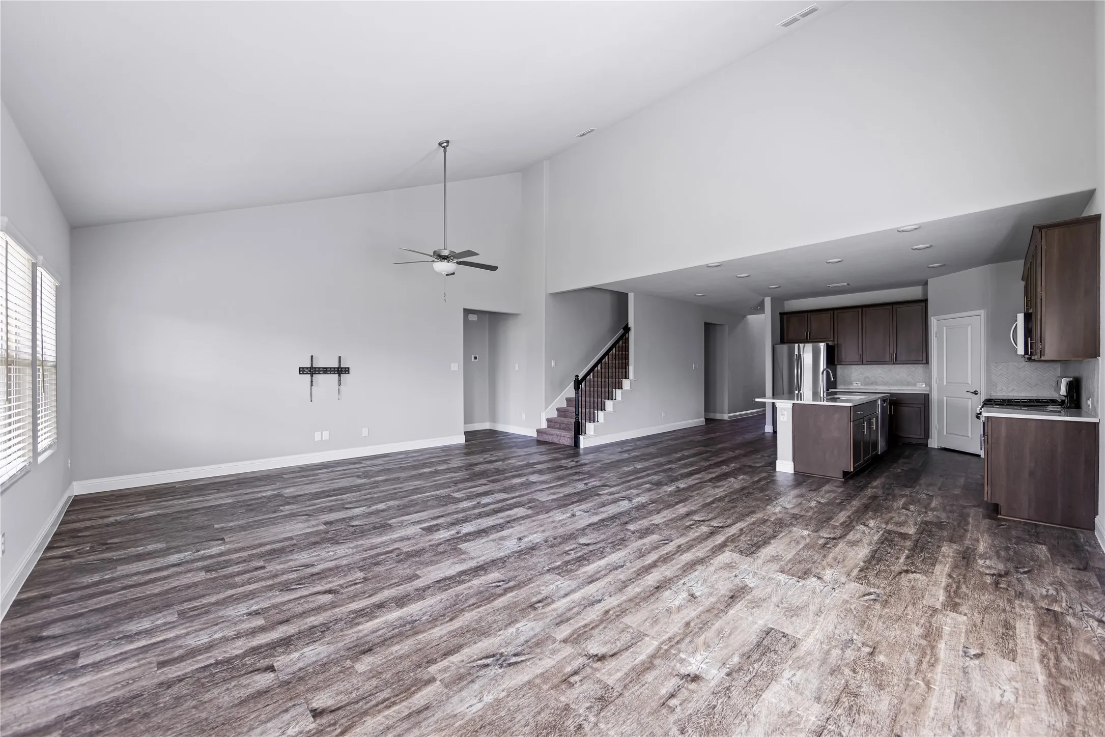 Vaulted ceilings, wood-finish flooring, staircase with metal balusters, and a kitchen featuring dark cabinetry and an island with seating