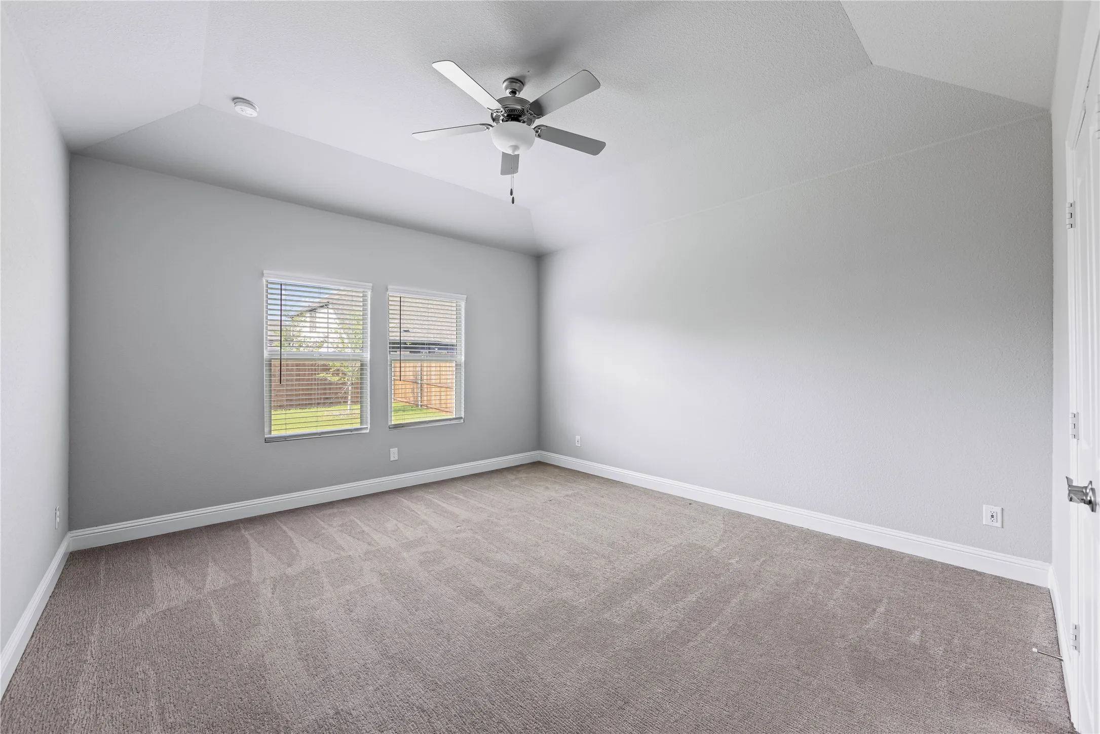 Vaulted ceiling with a ceiling fan, dual windows with blinds, neutral carpet flooring, and light-toned walls