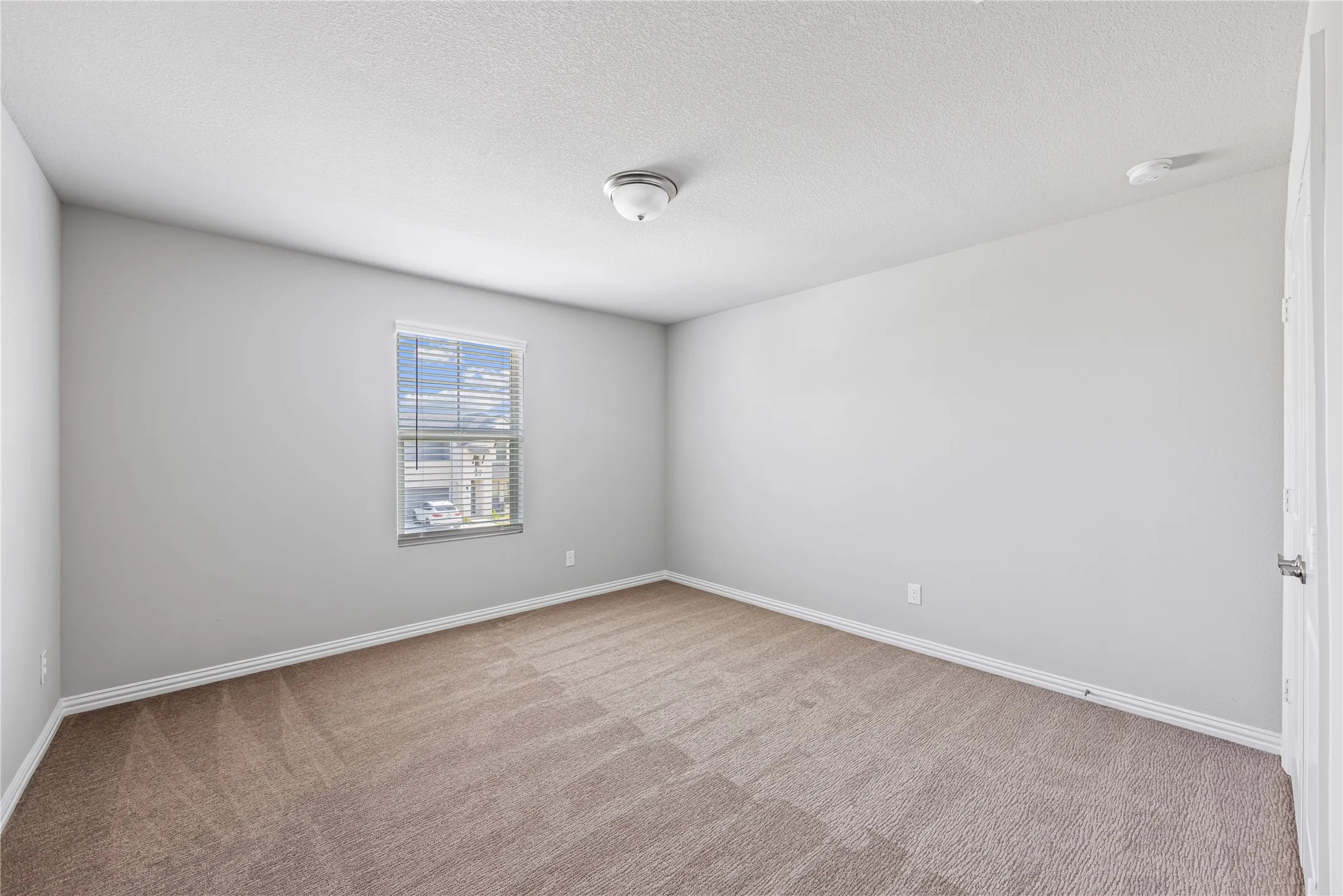 Recessed ceiling light, neutral wall paint, single window with blinds, carpeted flooring, white trim details
