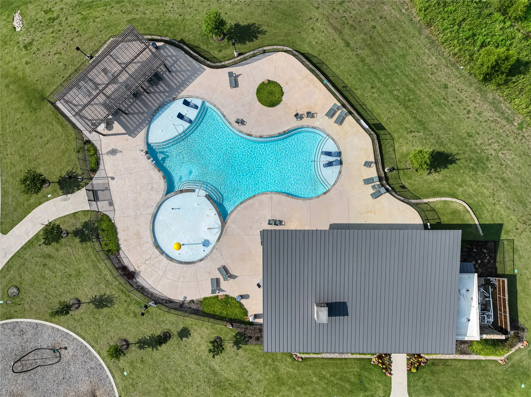 Resort-style pool with integrated splash pad, surrounding concrete decking, and a shaded pergola