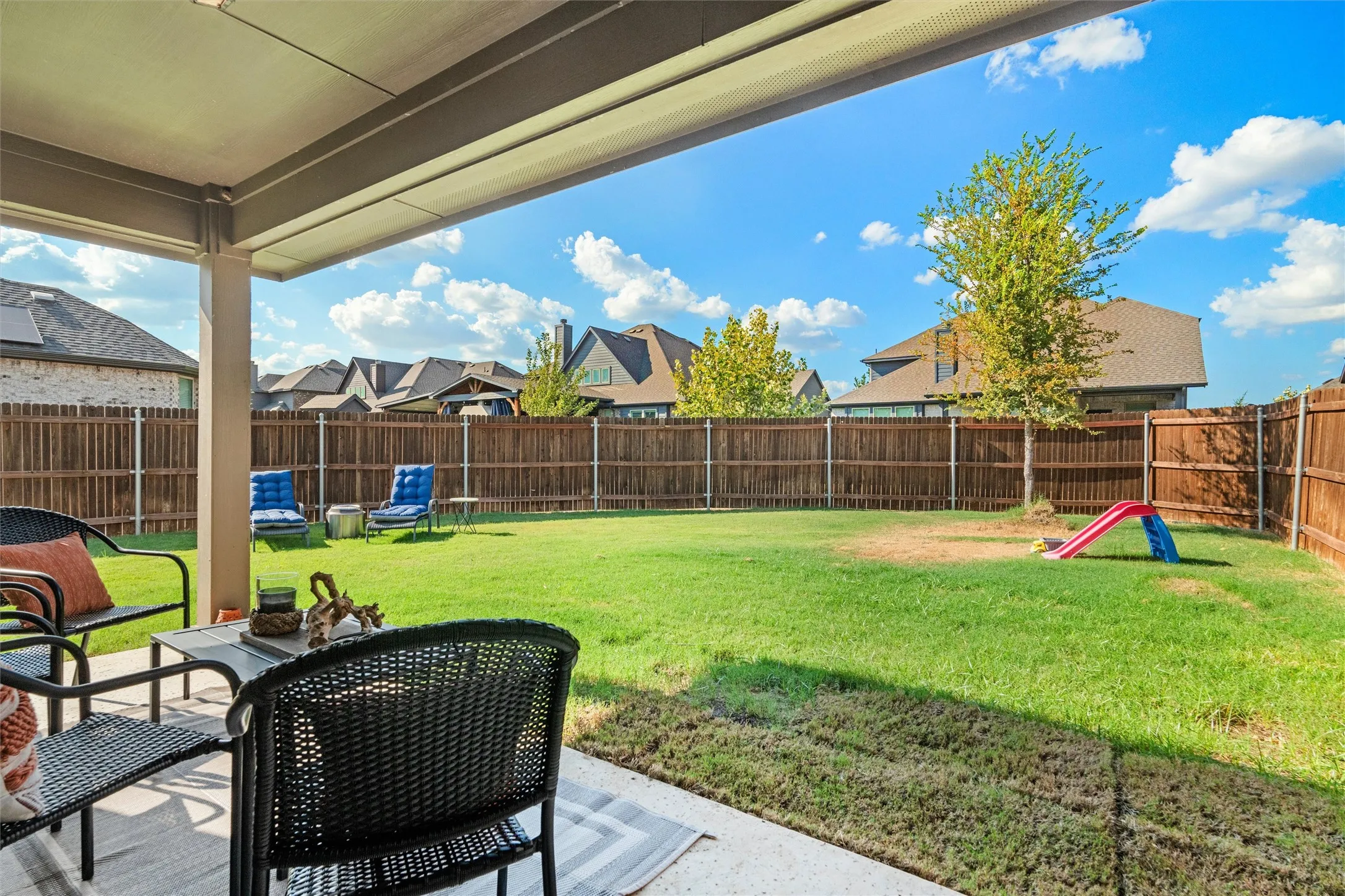 Expansive backyard featuring a manicured lawn, a wood privacy fence, and a covered patio