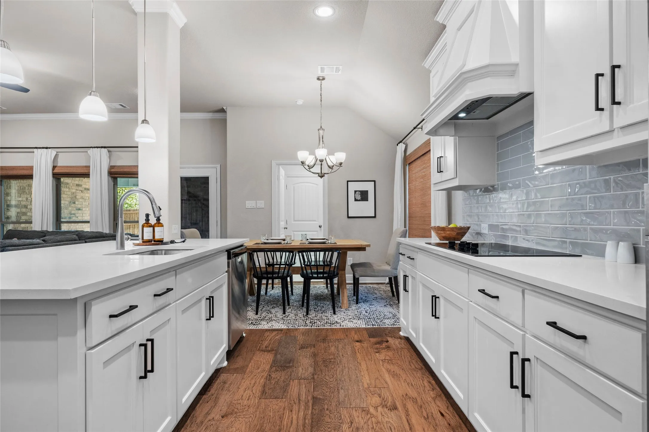 White shaker cabinetry with black hardware, light-toned countertops, tile backsplash, wood-finish flooring, and a built-in cooktop