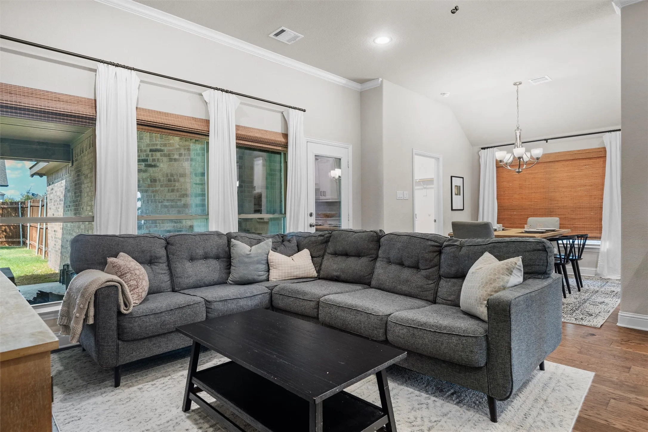 Vaulted ceiling, recessed lighting, wood-finish flooring, multiple windows with blinds, and crown molding