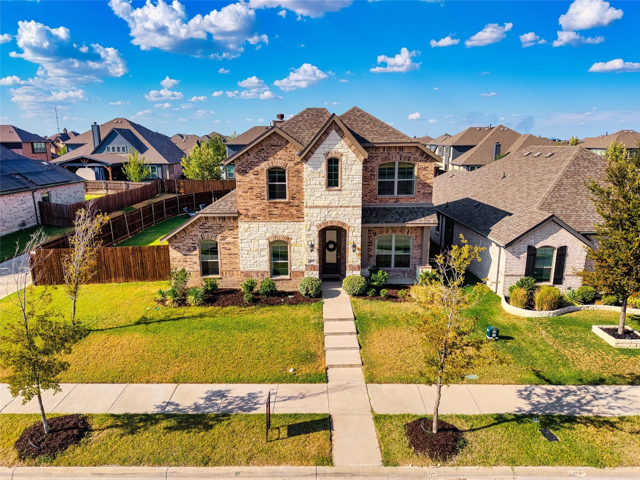 Two-story brick and stone facade, arched entry, gabled roof, established landscaping, and a concrete walkway