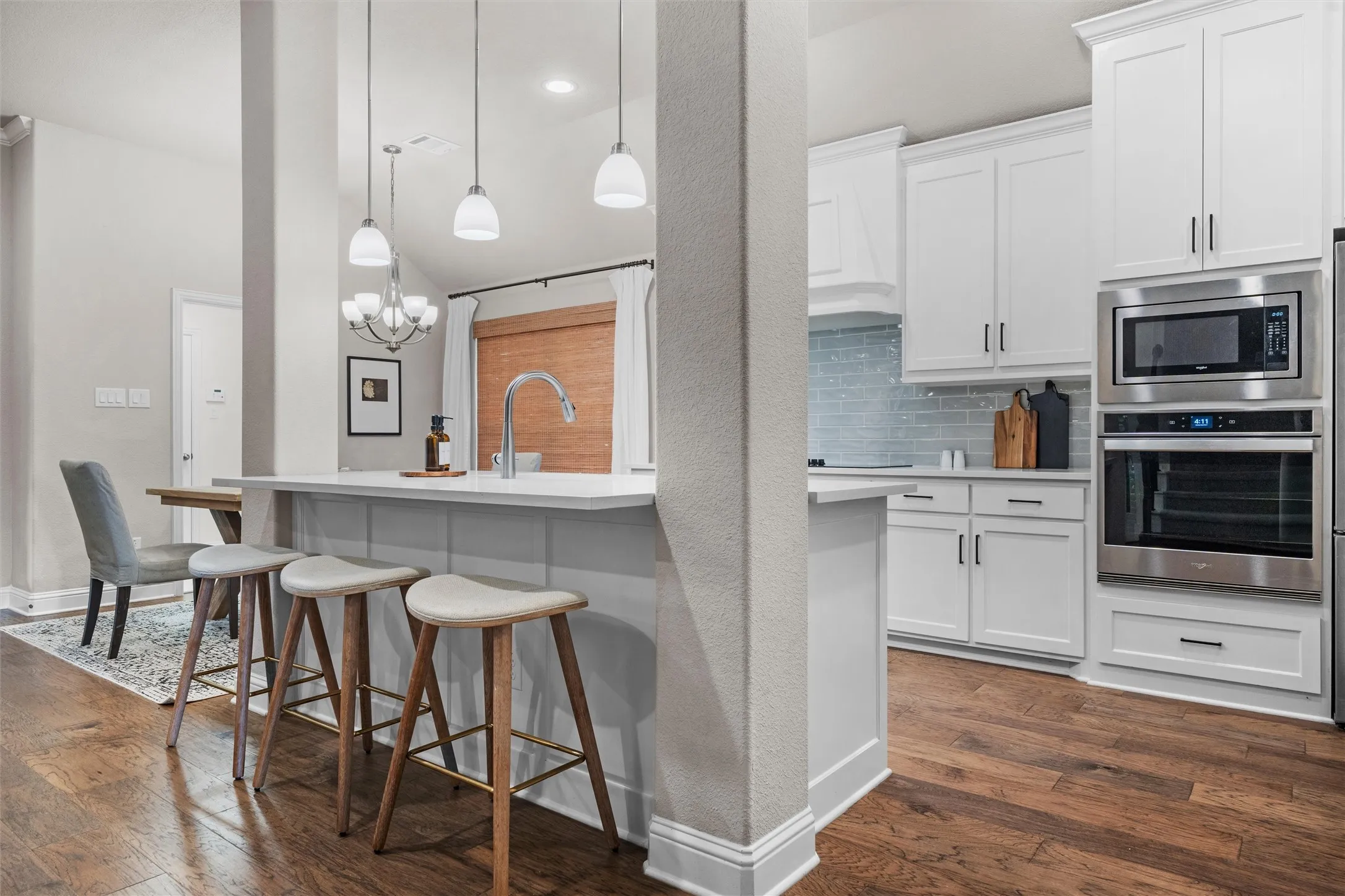 Kitchen featuring a central island with pendant lighting, wood-finish flooring, white cabinetry, and stainless steel built-in appliances