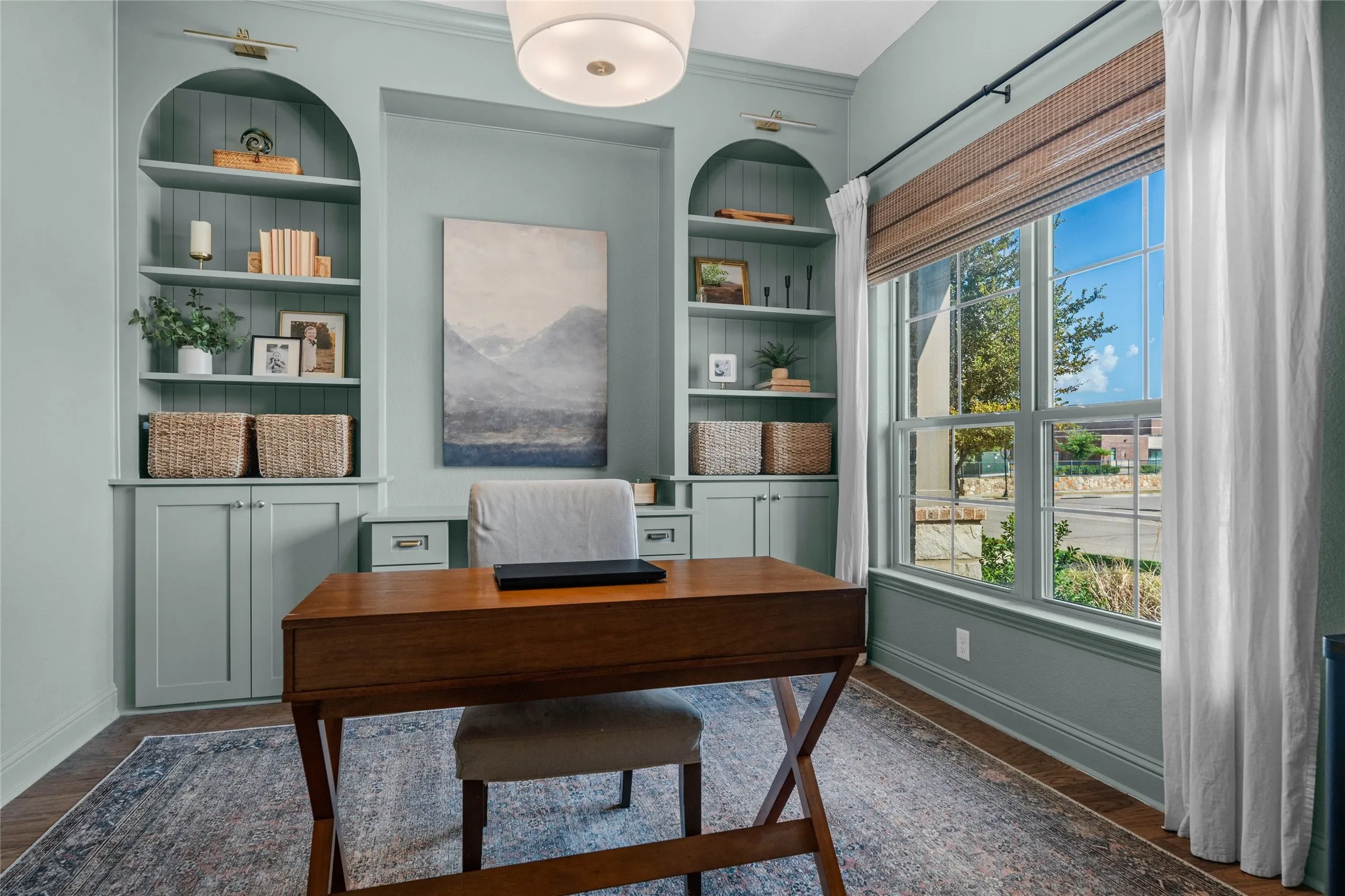 Built-in arched shelving with lower cabinetry, substantial window with natural light, wood-finish flooring, and overhead flush mount lighting