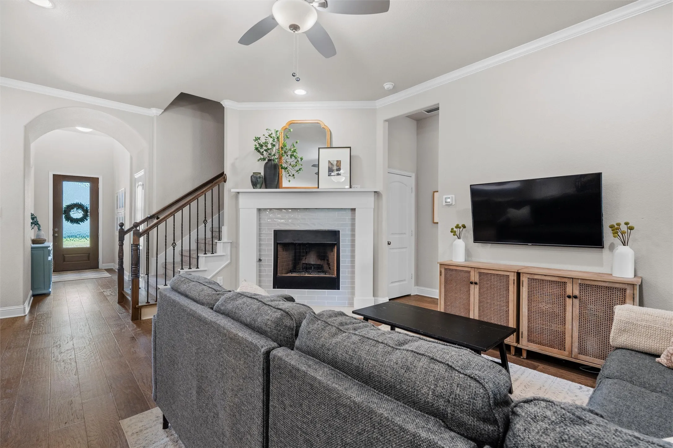 Living area featuring a fireplace with a white mantel and tile surround, wood-finish flooring, and a staircase with dark wood handrails and wrought iron balusters