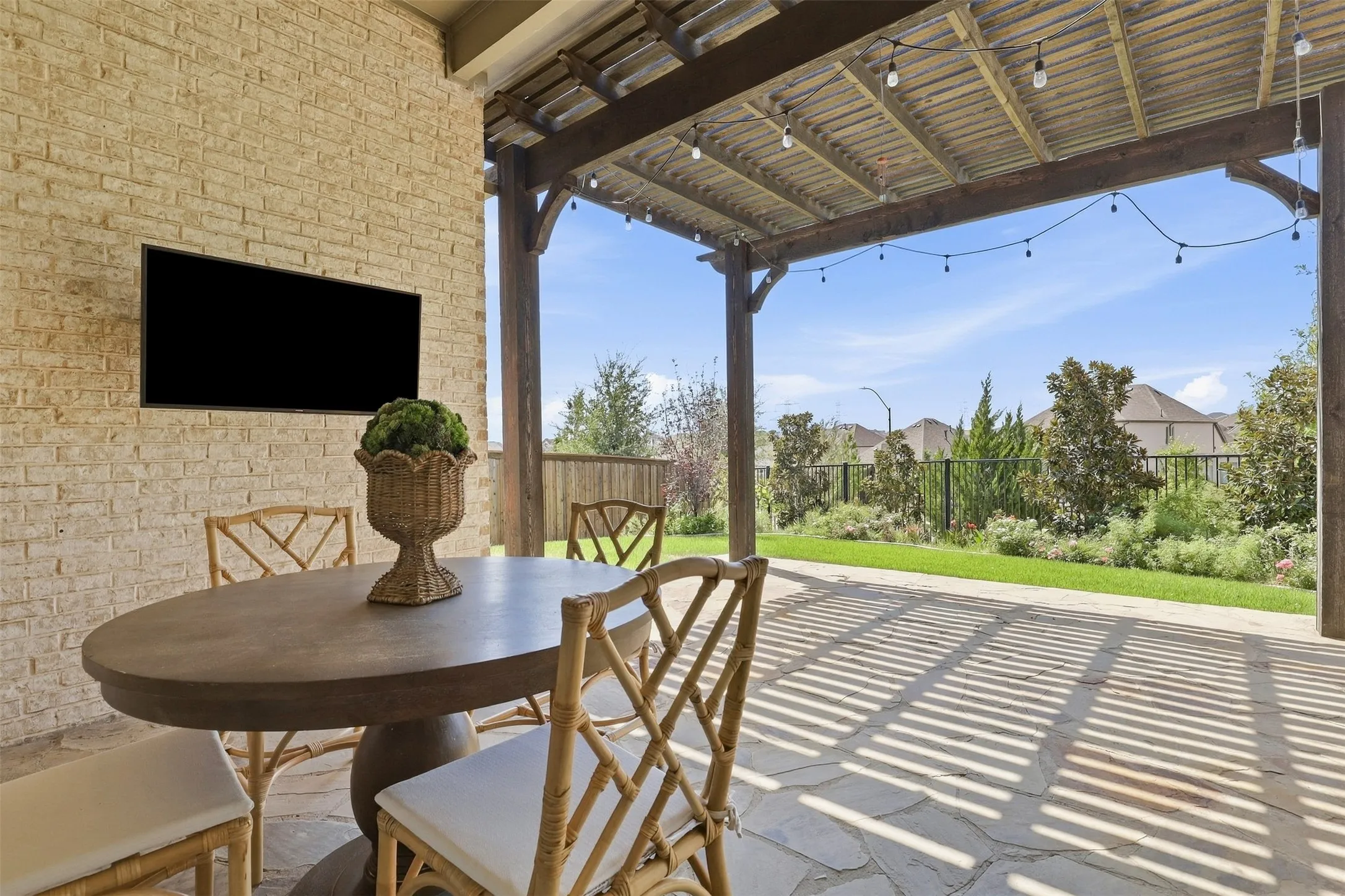 Covered outdoor patio featuring a flagstone surface, exposed beam ceiling, string lighting, and a mounted television