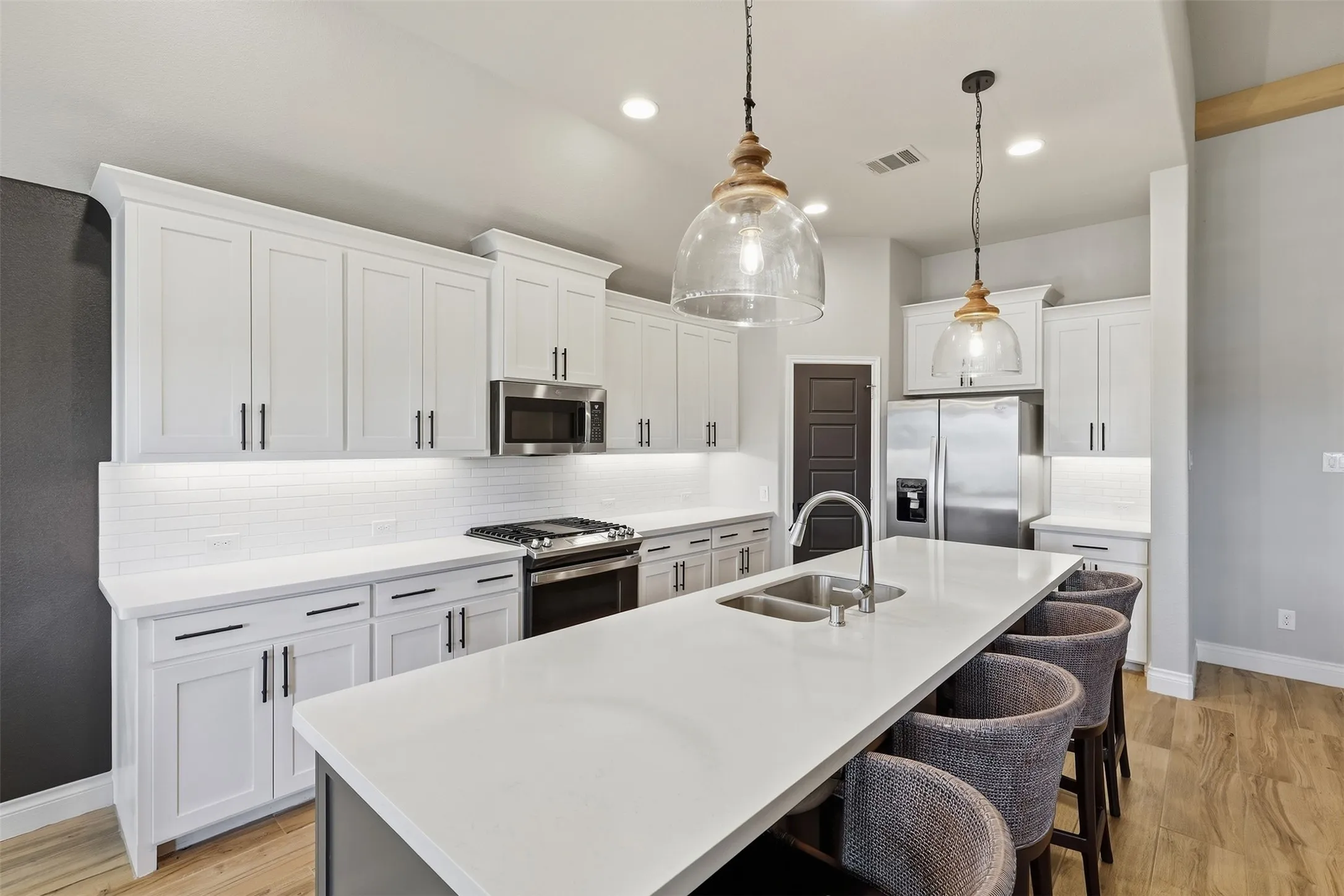 Gourmet kitchen featuring white shaker cabinetry, stainless steel appliances, a large center island with a double basin sink, and wood-finish flooring