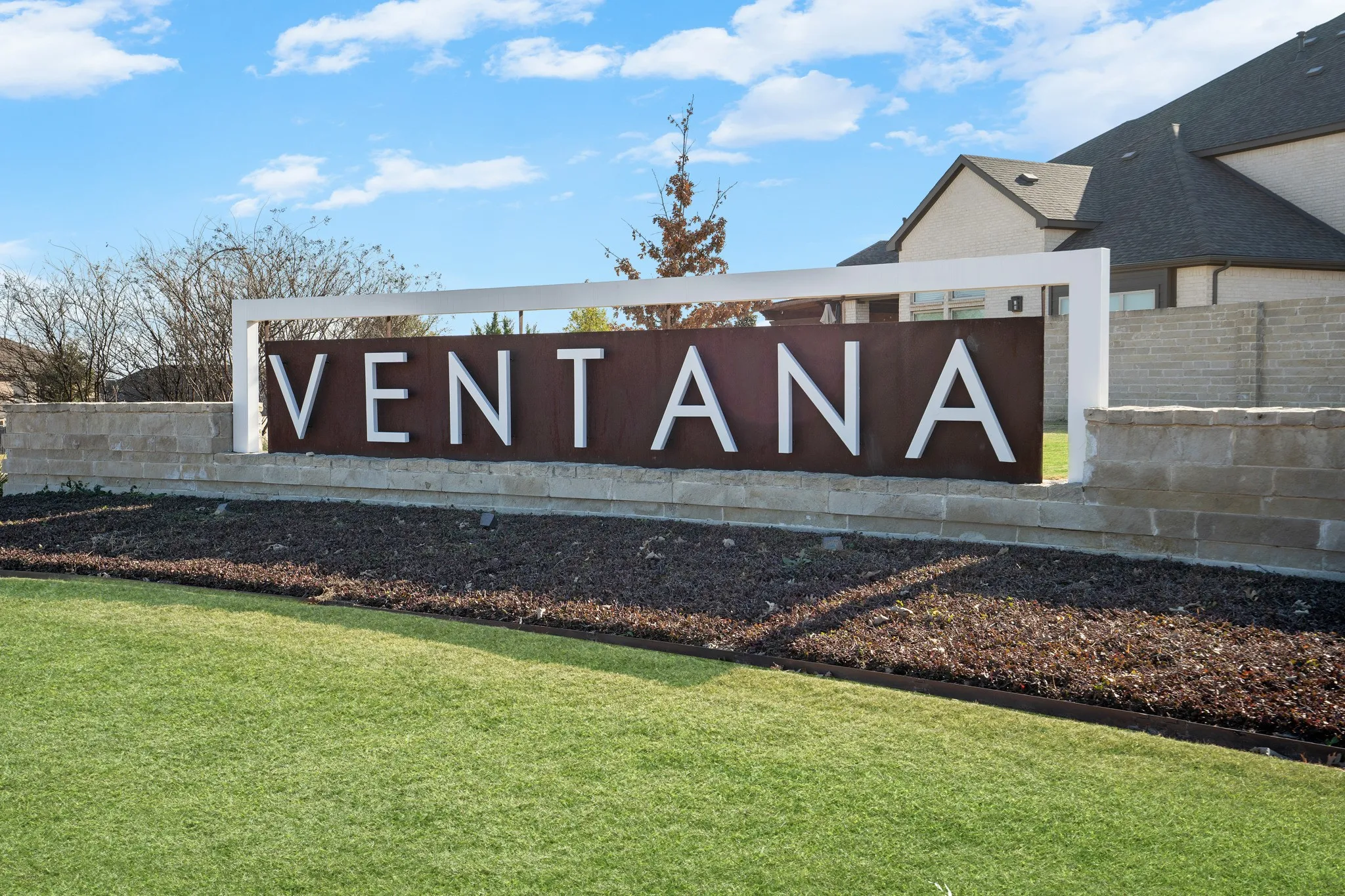 Ventana community signage featuring a stone base and metal lettering, surrounded by manicured lawn and landscaping