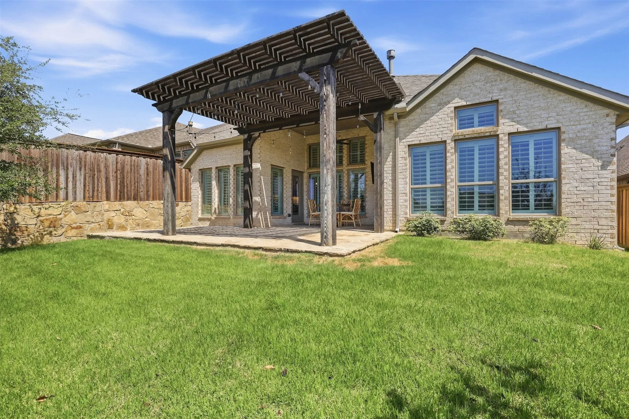 Expansive backyard featuring a stone exterior, wood pergola, and large windows with plantation shutters