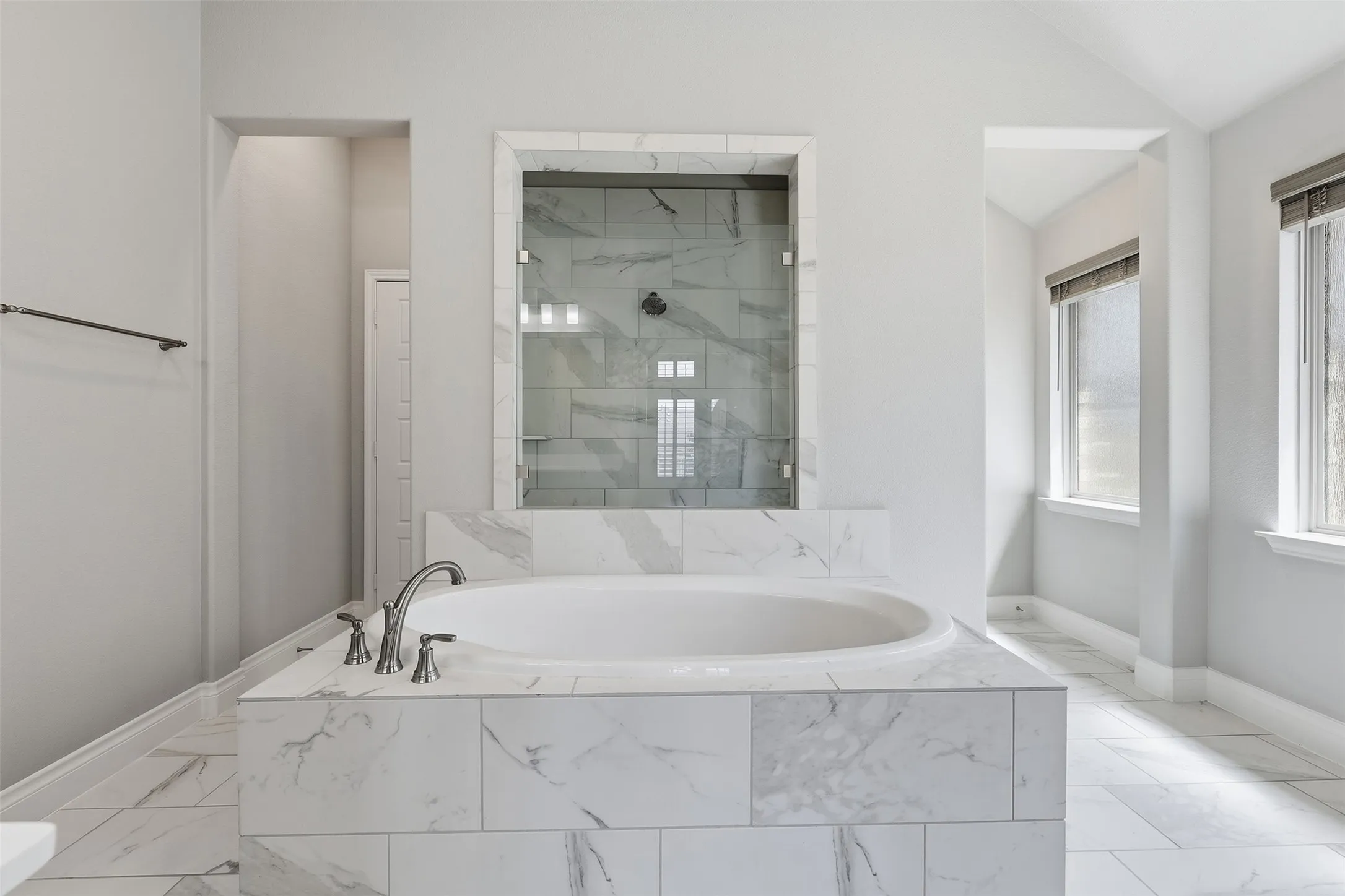 Soaking tub with brushed nickel fixtures, glass-enclosed shower with tiled walls, and white tiled flooring