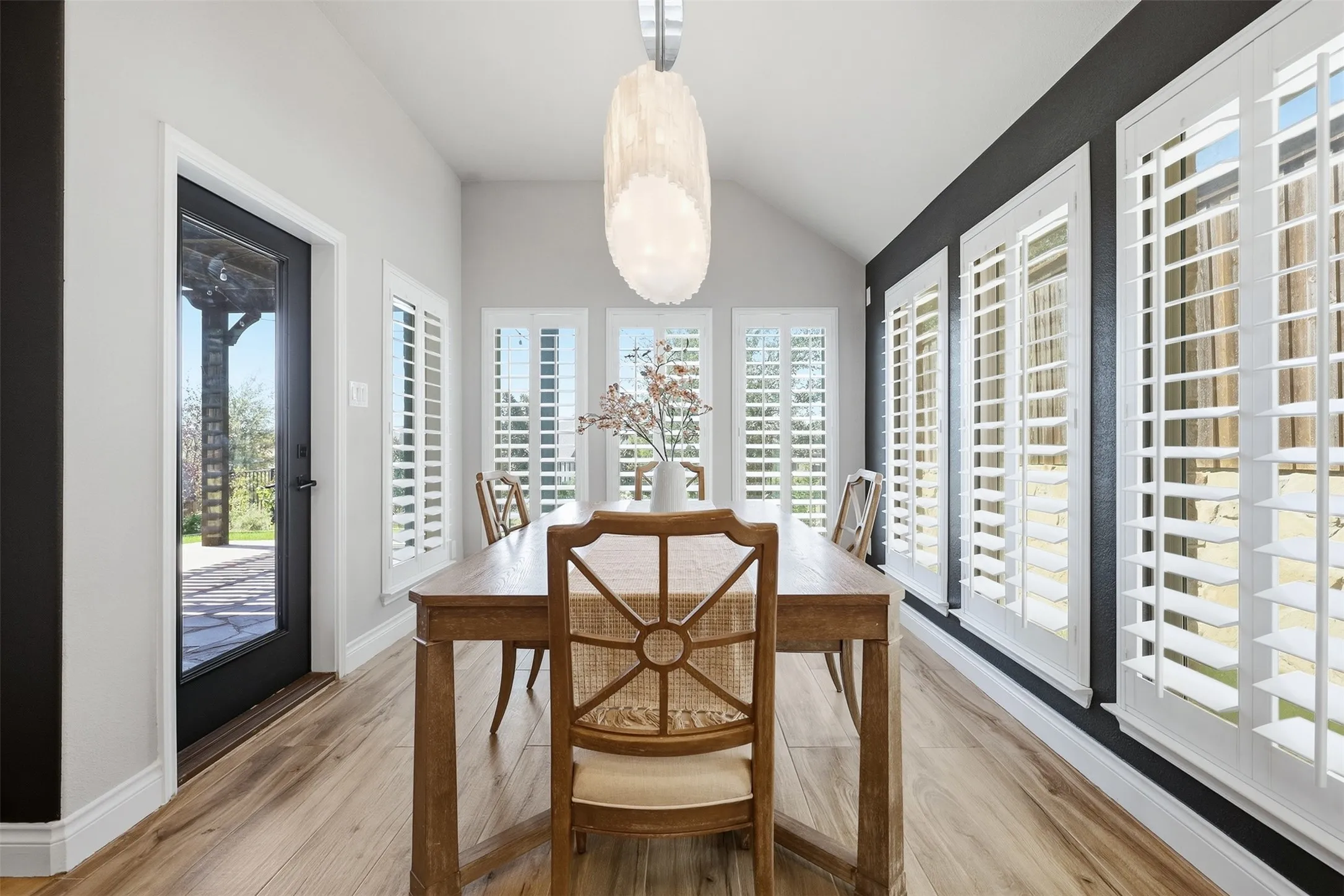 Vaulted ceiling with an elegant pendant light fixture, wood-finish flooring, and multiple windows with plantation shutters