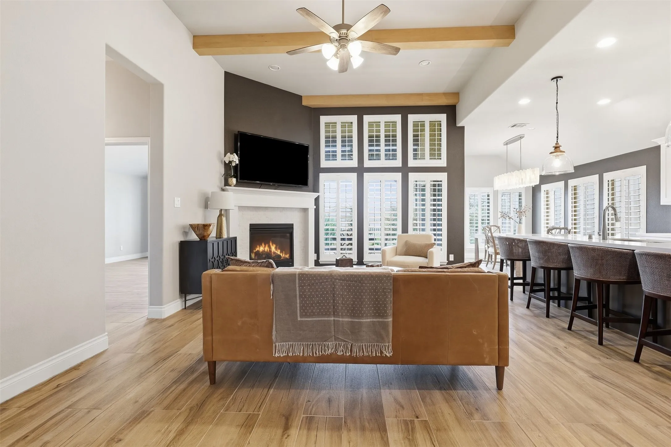 Open-concept living area with wood-finish flooring, a fireplace with a white mantel, and extensive window shutters