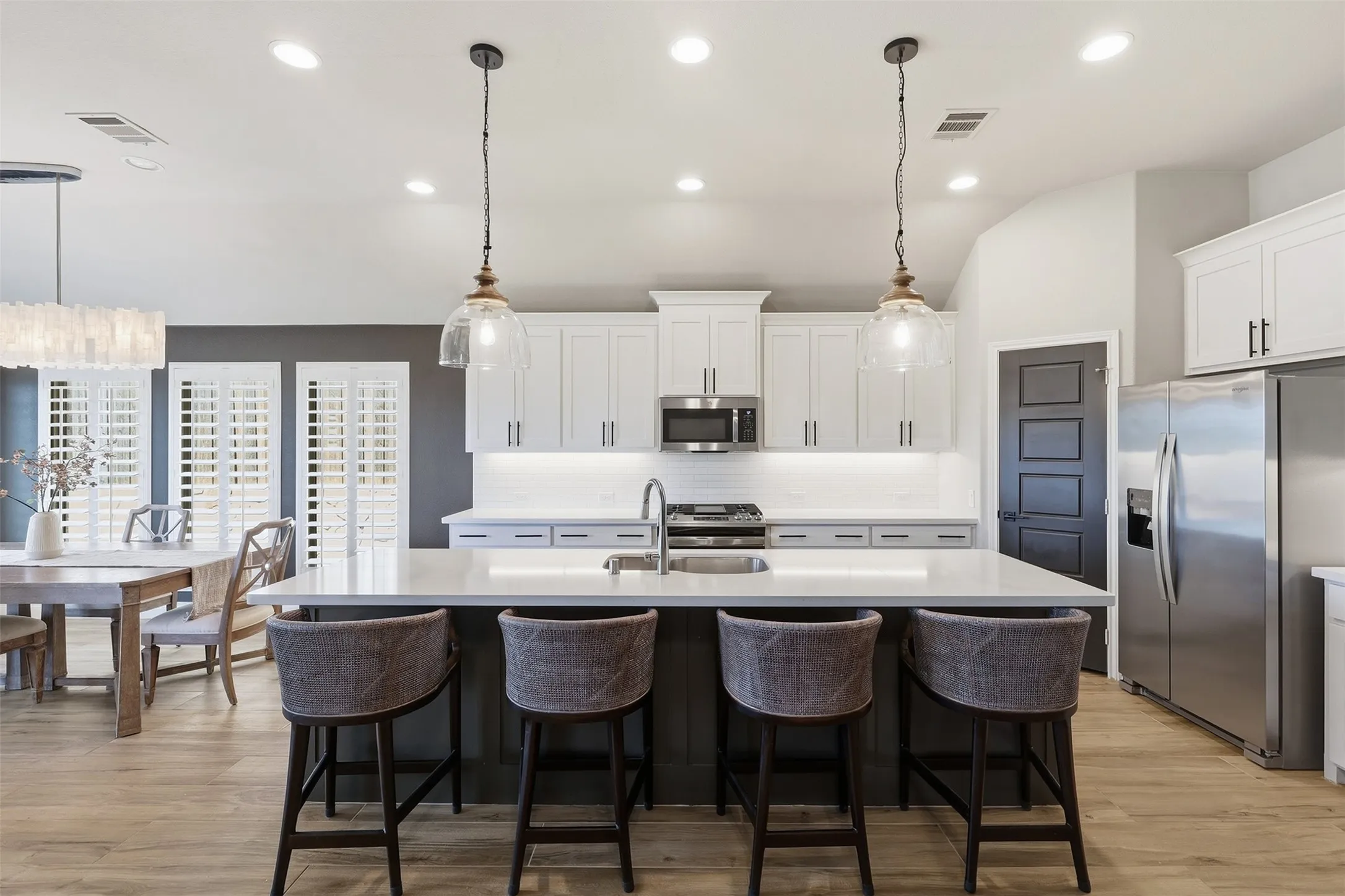 Kitchen island with a light-toned countertop, stainless steel appliances, white cabinetry, wood-finish flooring, and pendant lighting