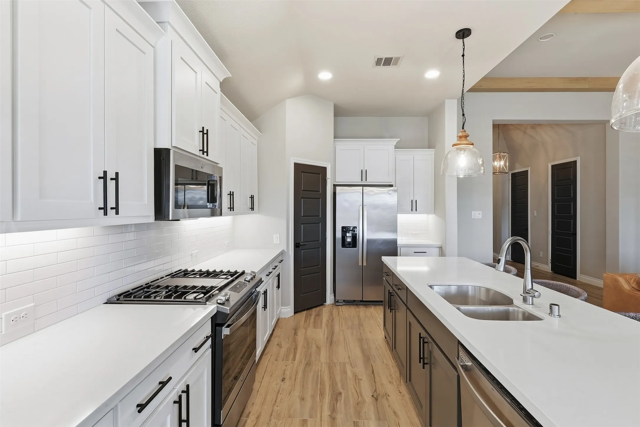 White shaker cabinetry with black hardware, stainless steel appliances, white subway tile backsplash, light wood-finish flooring, and a kitchen island with an undermount double sink