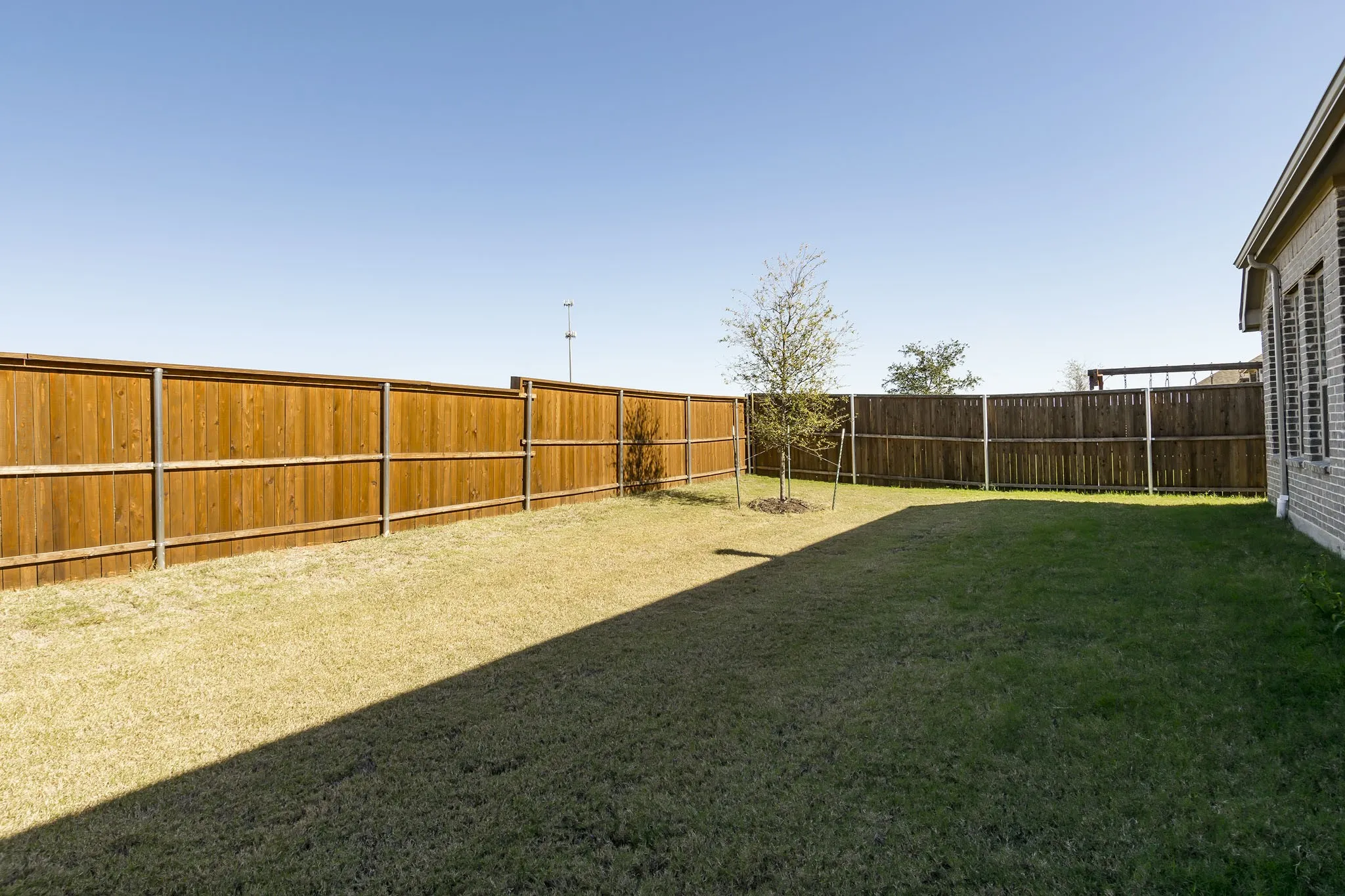 Expansive backyard featuring a level lawn with mature landscaping, sturdy wood-finish fencing, and clear sightlines to additional residential structures on the property