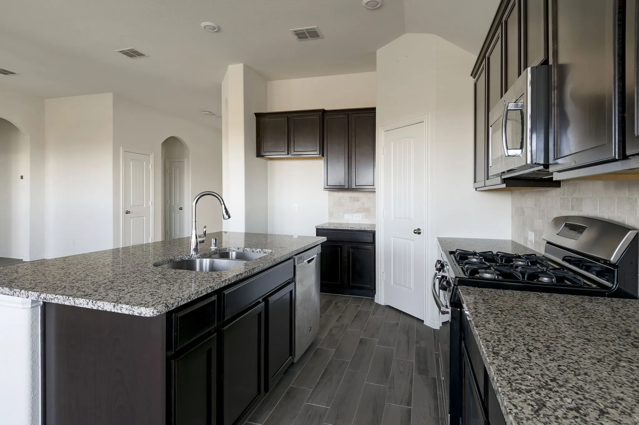 Spacious kitchen featuring granite countertops, dark wood cabinetry, a stainless steel gas range, and a large island with an undermount sink