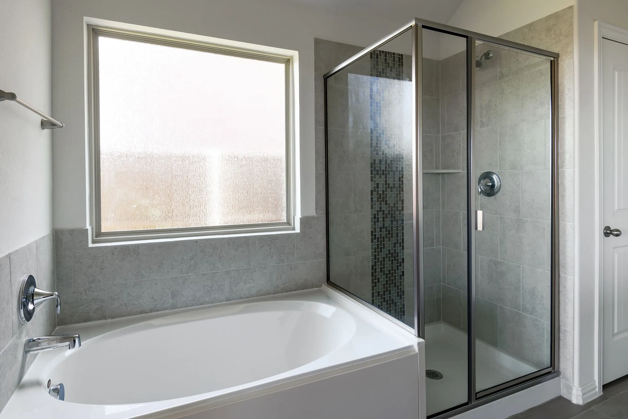 Soaking tub with chrome fixtures, tiled shower with glass enclosure, mosaic tile accent, built-in shower shelf, and frosted window