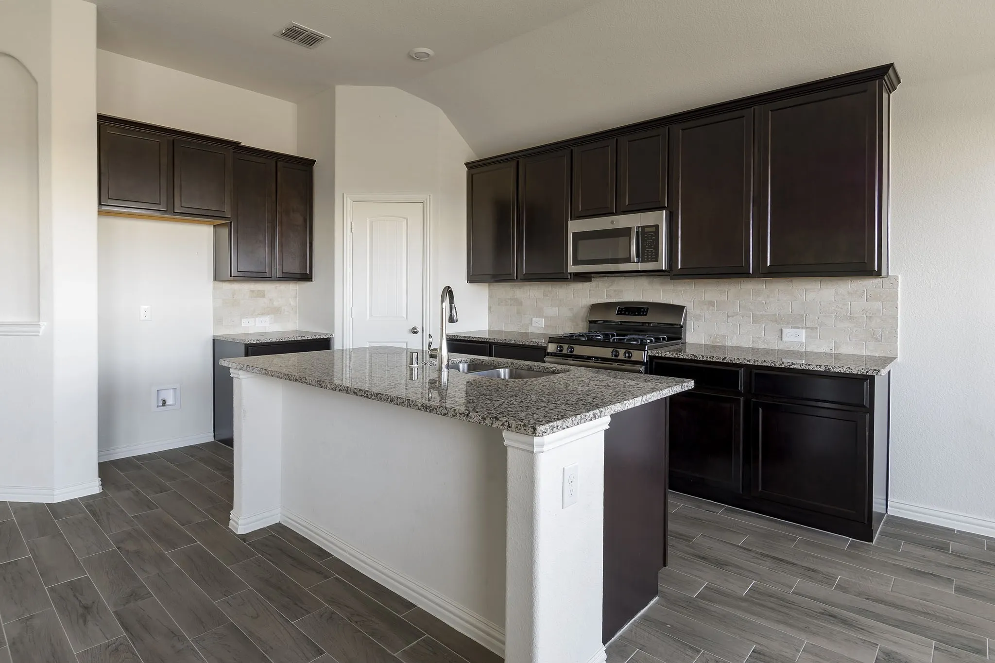 Spacious kitchen featuring an island with a sink, dark wood-finish cabinetry, granite countertops, and stainless steel appliances
