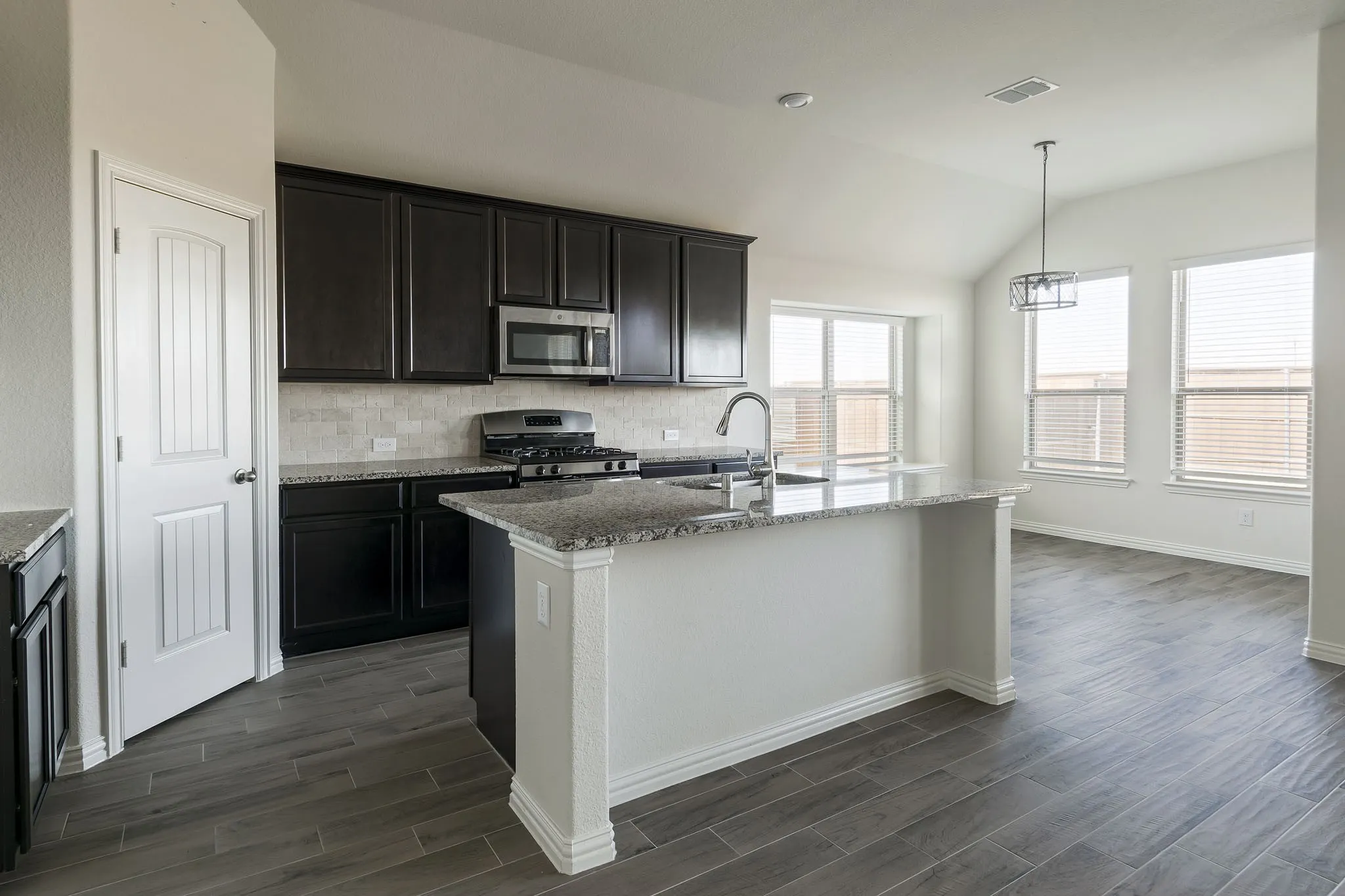 Kitchen featuring dark wood cabinetry, stainless steel appliances, granite countertops, tile backsplash, and a central island with an undermount sink