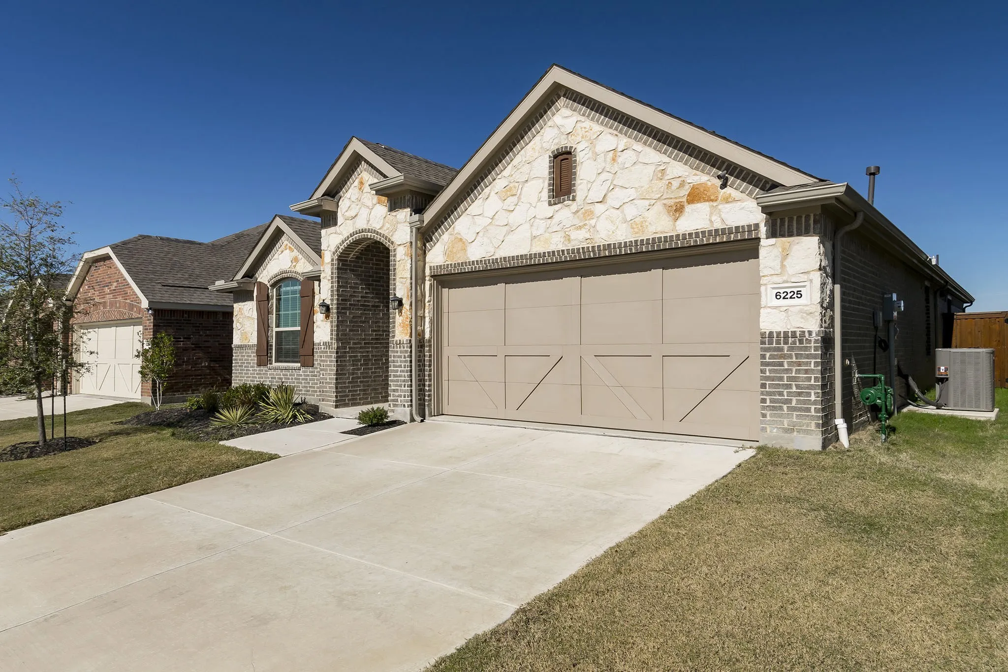 Exterior featuring stone and brick facade, arched entry, decorative garage door, concrete driveway, and landscaped front yard