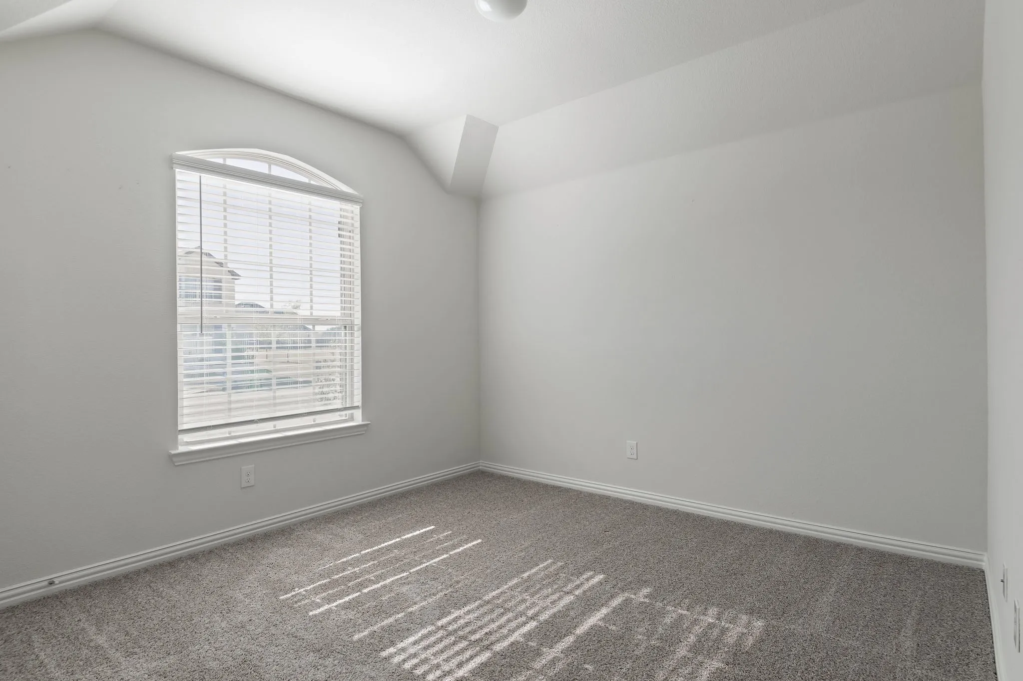 Arched window with blinds, vaulted ceiling, neutral wall tones, and gray carpeting