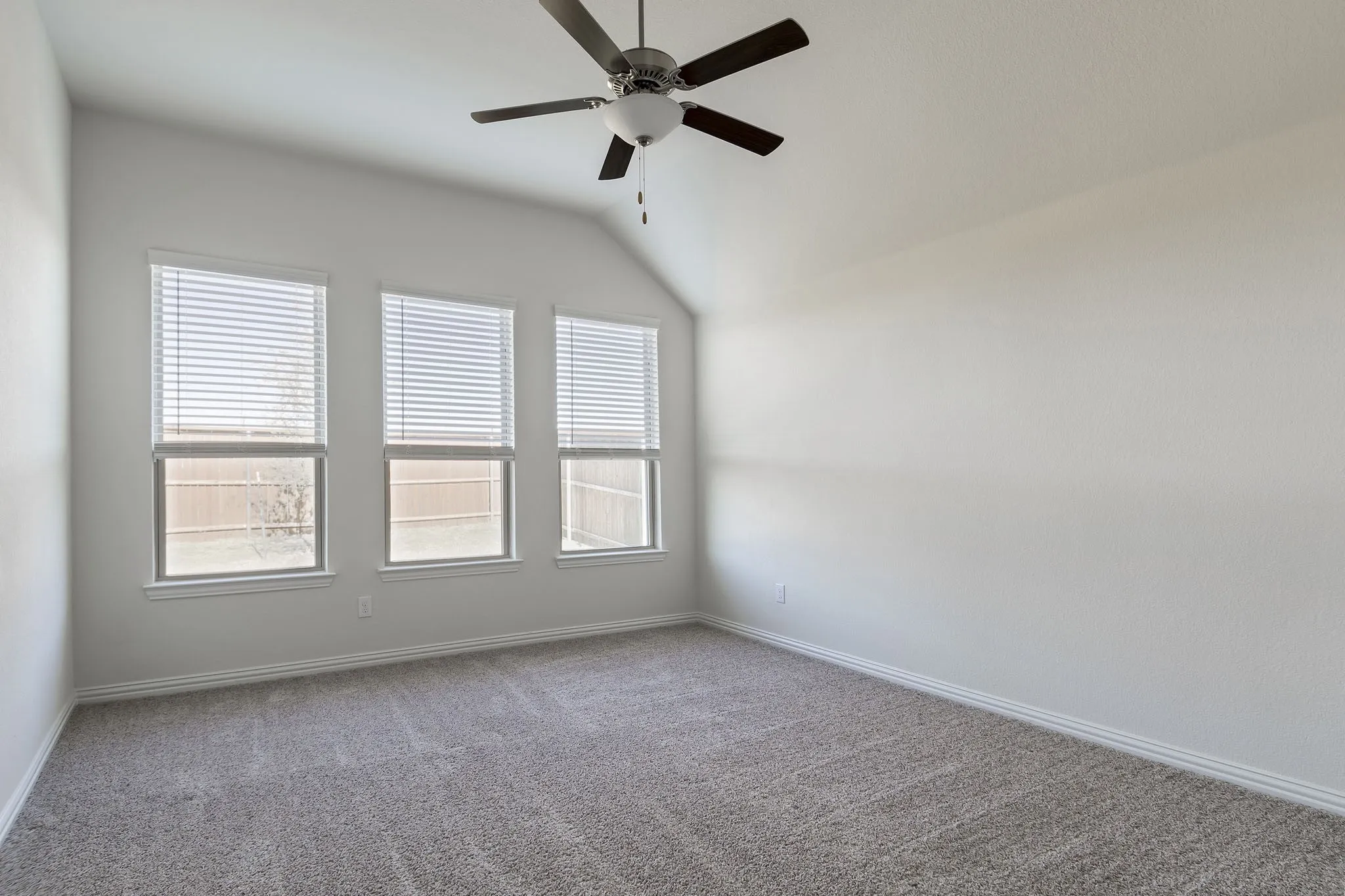 Vaulted ceiling with a ceiling fan, three windows with blinds, and neutral carpeting