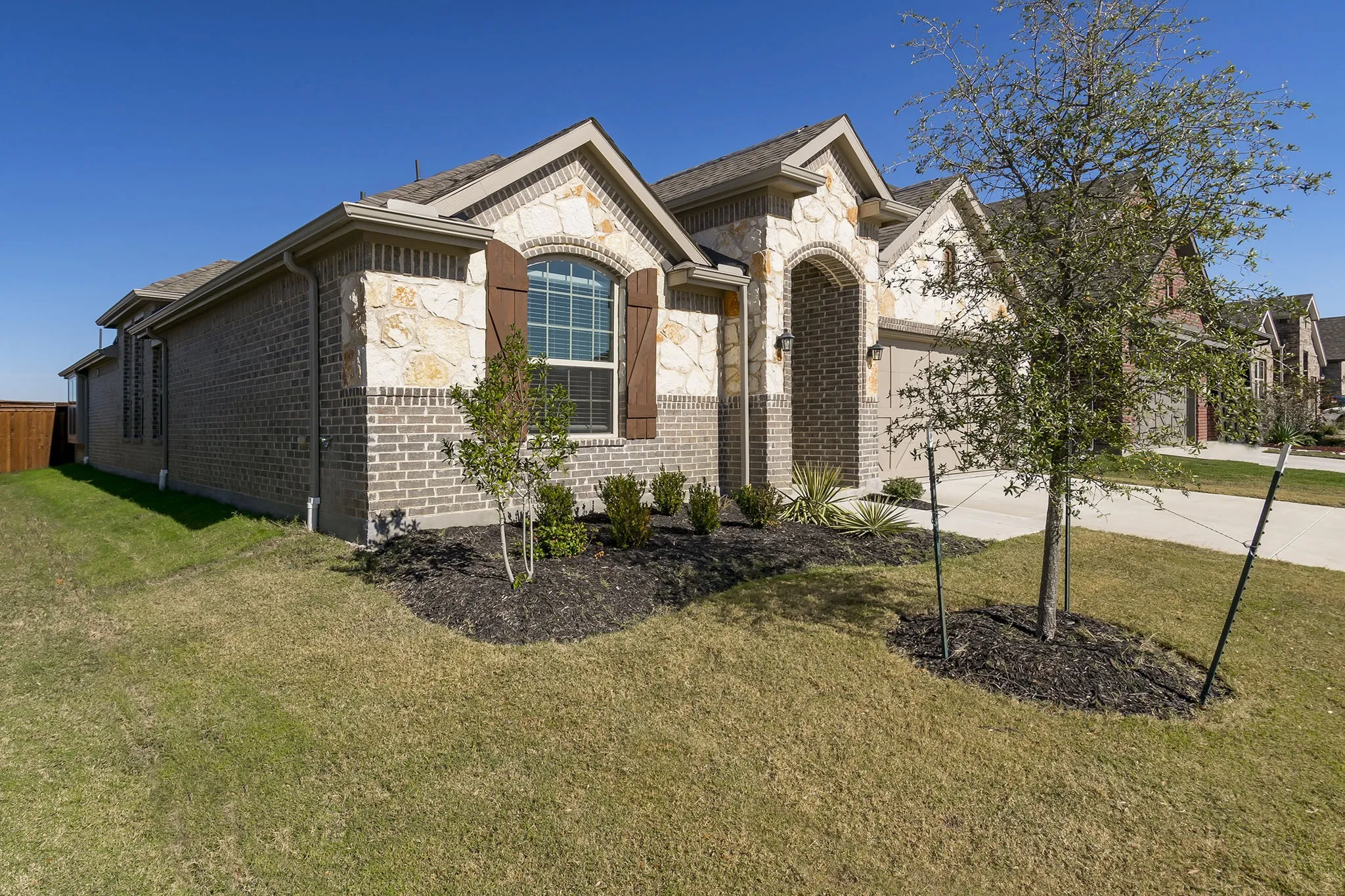 Brick and stone facade with arched window, decorative shutters, and mature landscaping