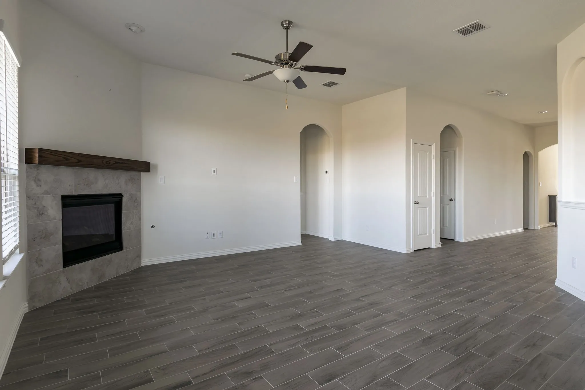 Living area with a corner fireplace featuring a wood mantel, tile surround, and a ceiling fan