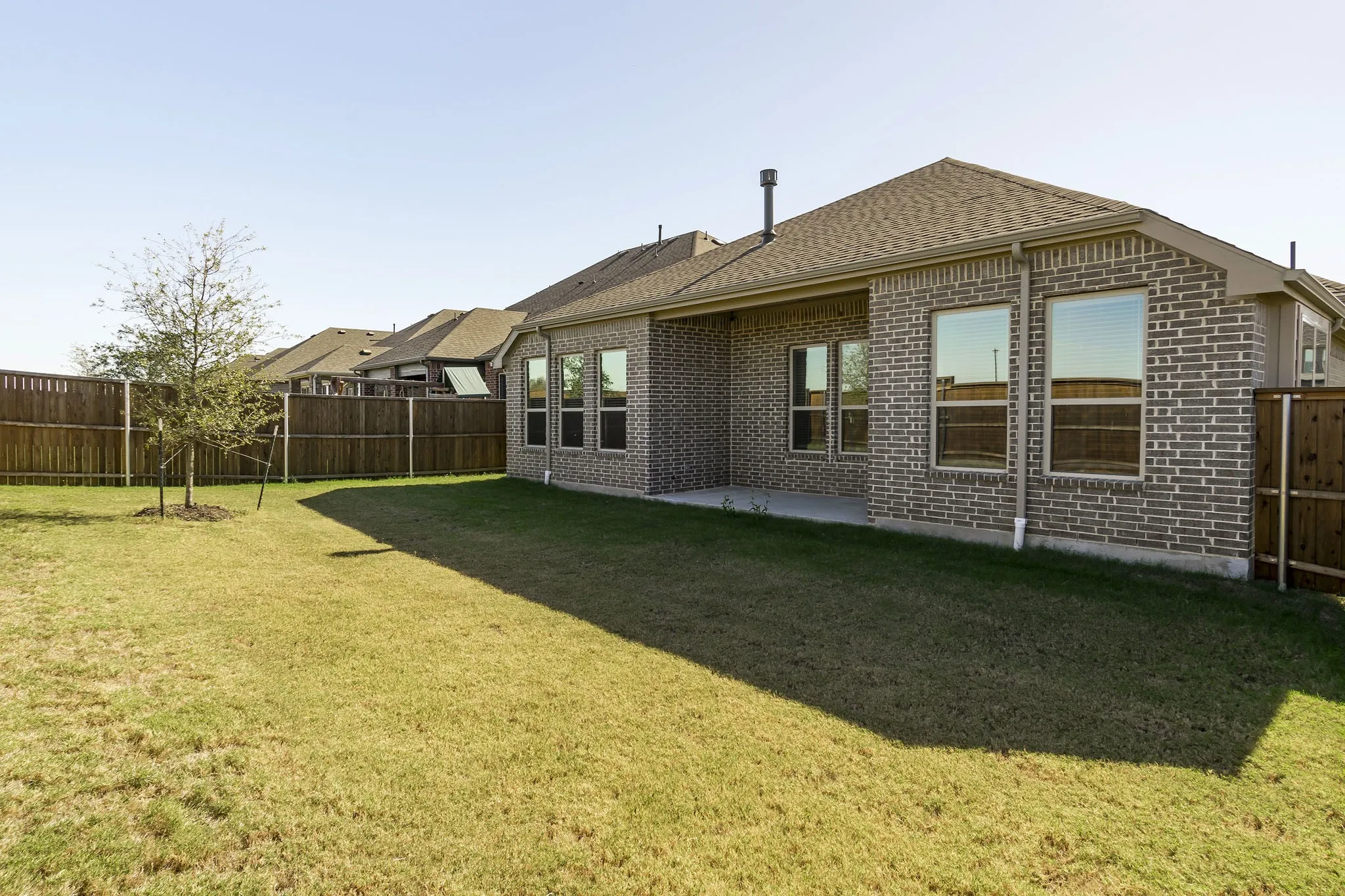 Expansive backyard with a manicured lawn, full brick exterior, large windows, covered patio, and privacy fencing