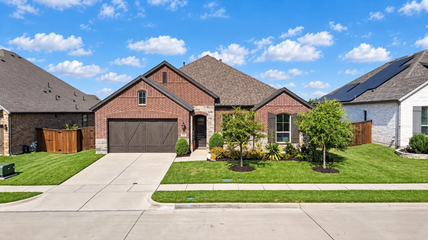 Brick facade with stone accents, attached two-car garage, concrete driveway, and a landscaped front yard