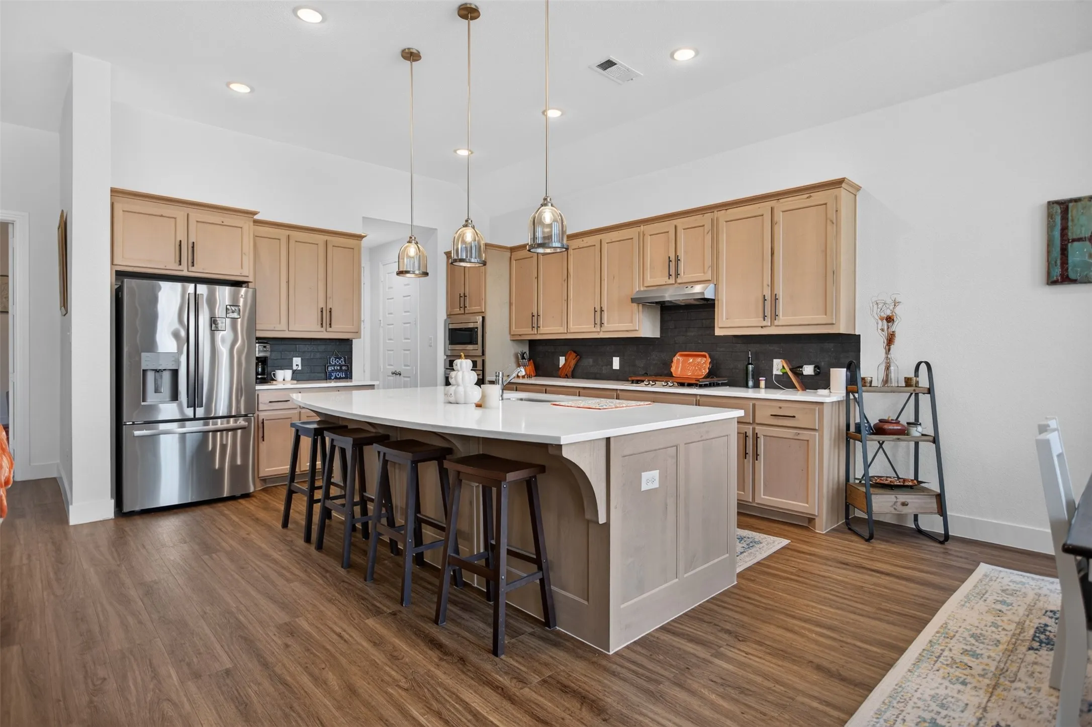 Spacious kitchen featuring an expansive center island, stainless steel appliances, wood-finish flooring, recessed lighting, and a dark tile backsplash