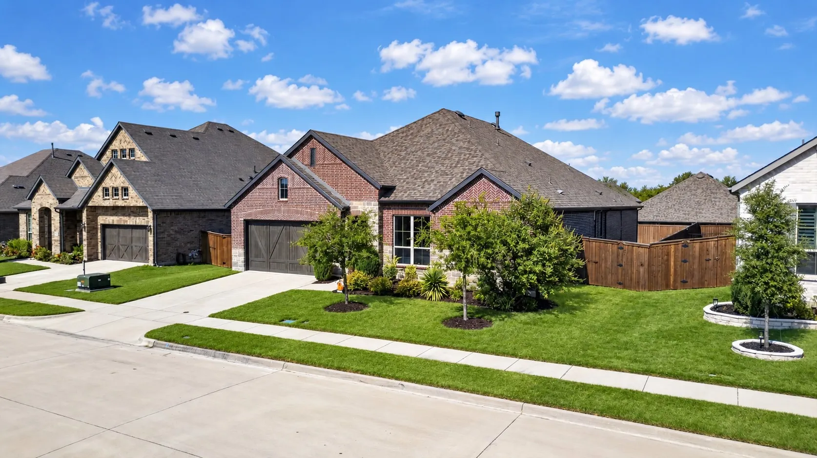 Brick facade with stone accents, attached two-car garage, concrete driveway, and a landscaped front yard