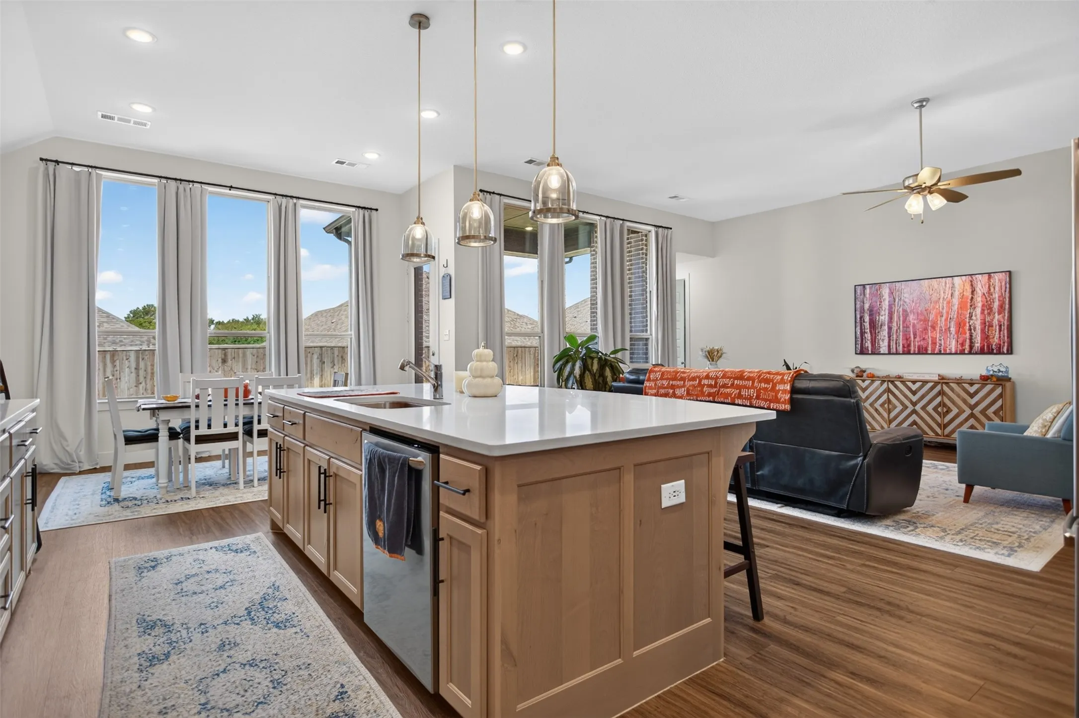 Spacious open-concept layout featuring a kitchen island with pendant lighting, a dining area with multiple windows, and wood-finish flooring throughout