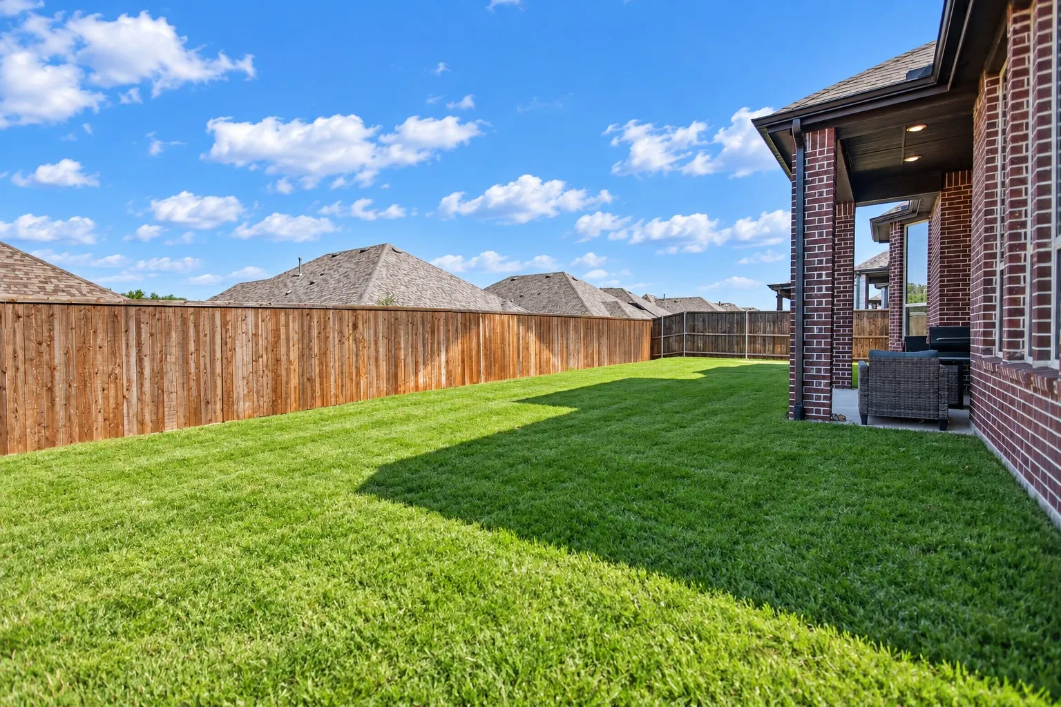 Expansive backyard featuring a manicured lawn, wood privacy fencing, and a covered patio with recessed lighting