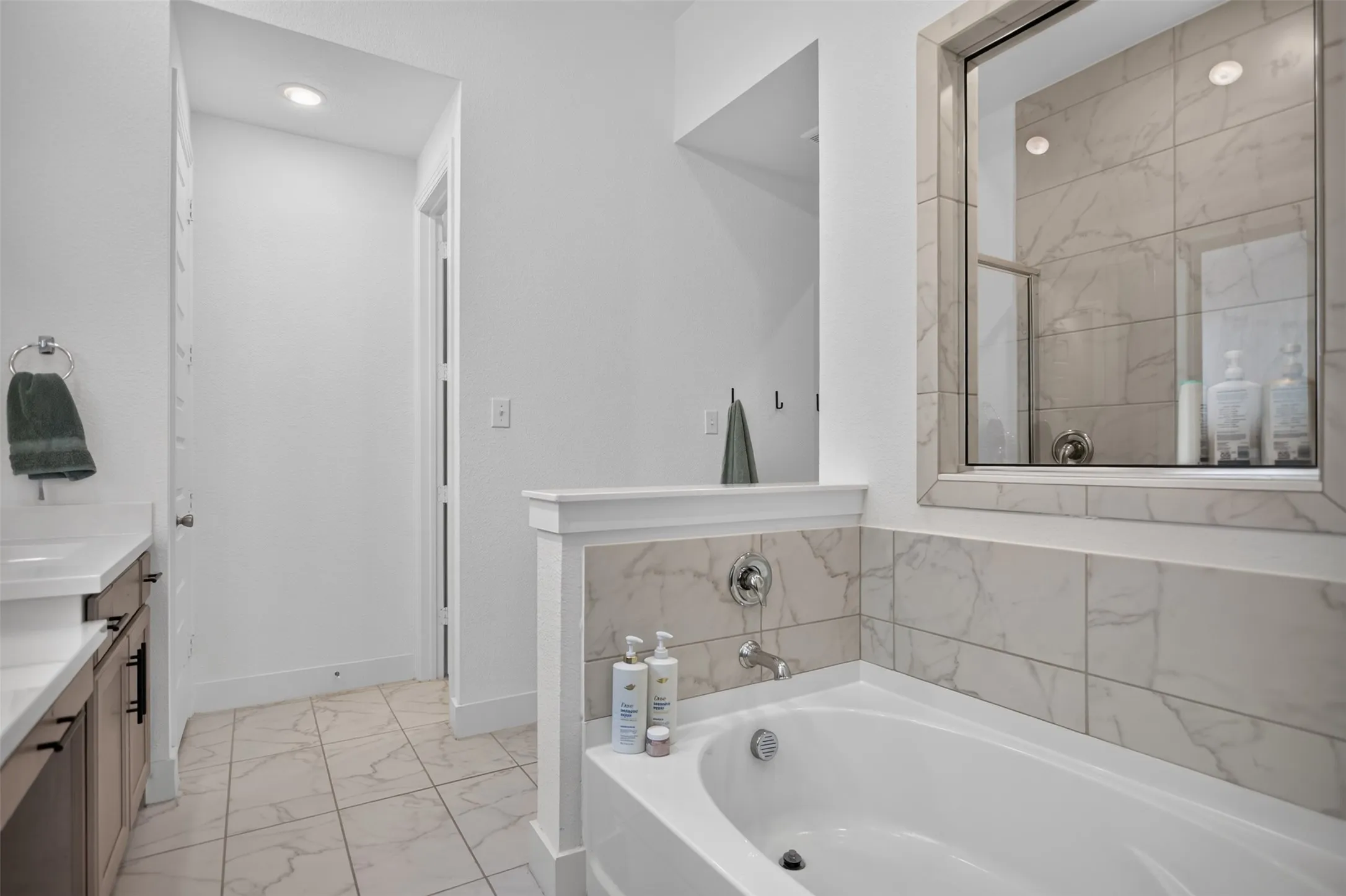 Built-in soaking tub, glass-enclosed shower, tiled walls, recessed lighting, and a vanity with an undermount sink