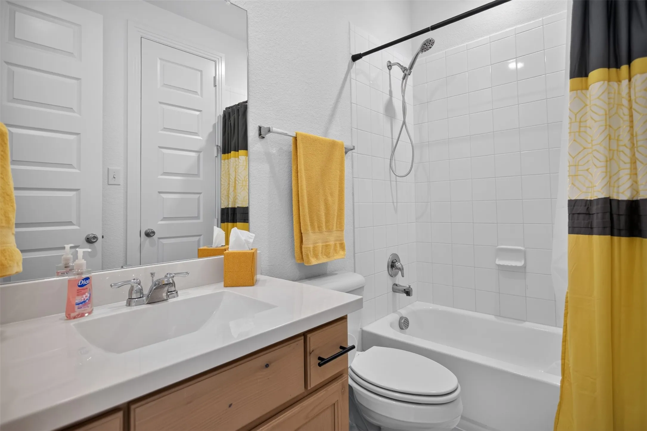 White tile tub/shower combination, single vanity with integrated sink, wood-finish cabinetry, and full-width mirror