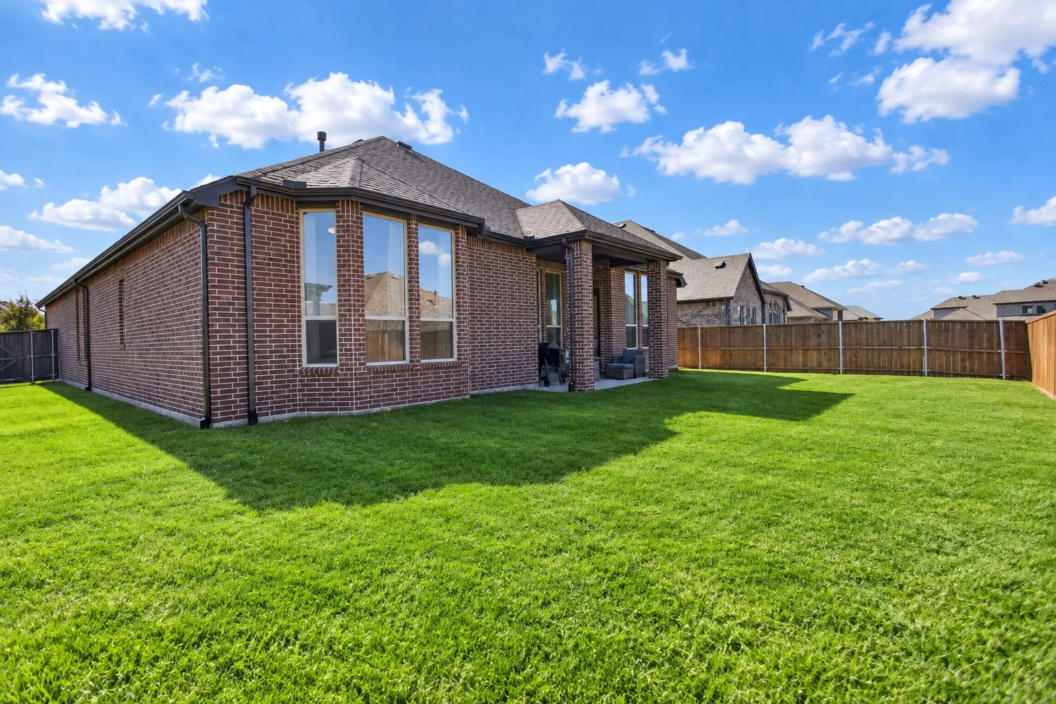 Expansive backyard with a manicured lawn, full privacy fencing, and a covered patio area