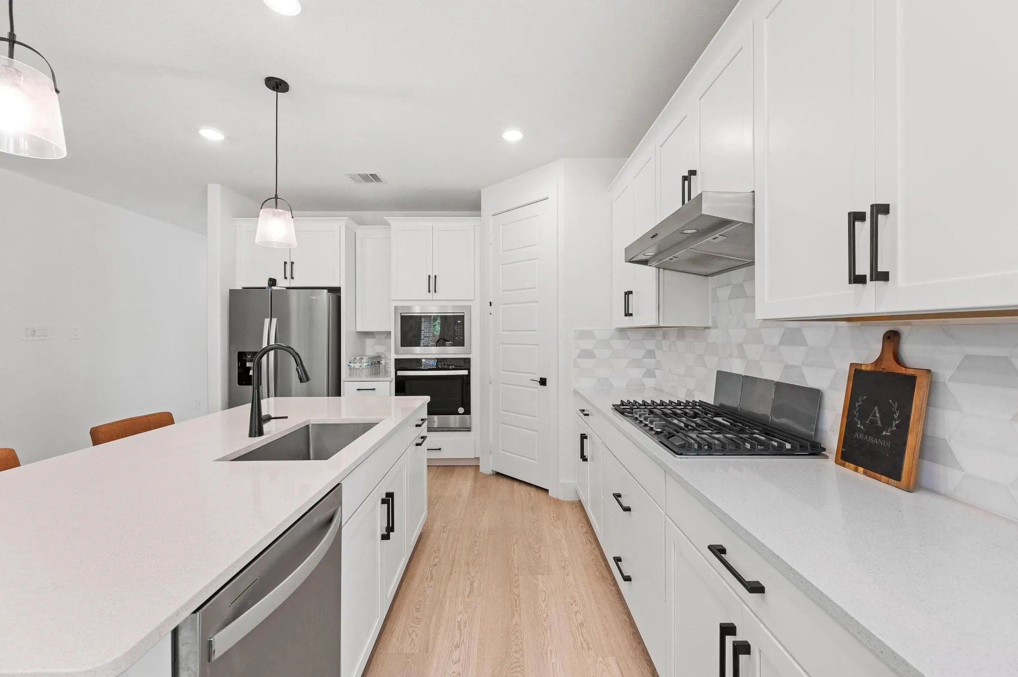 White kitchen cabinetry with black hardware, light wood-finish flooring, stainless steel appliances, and a gas range