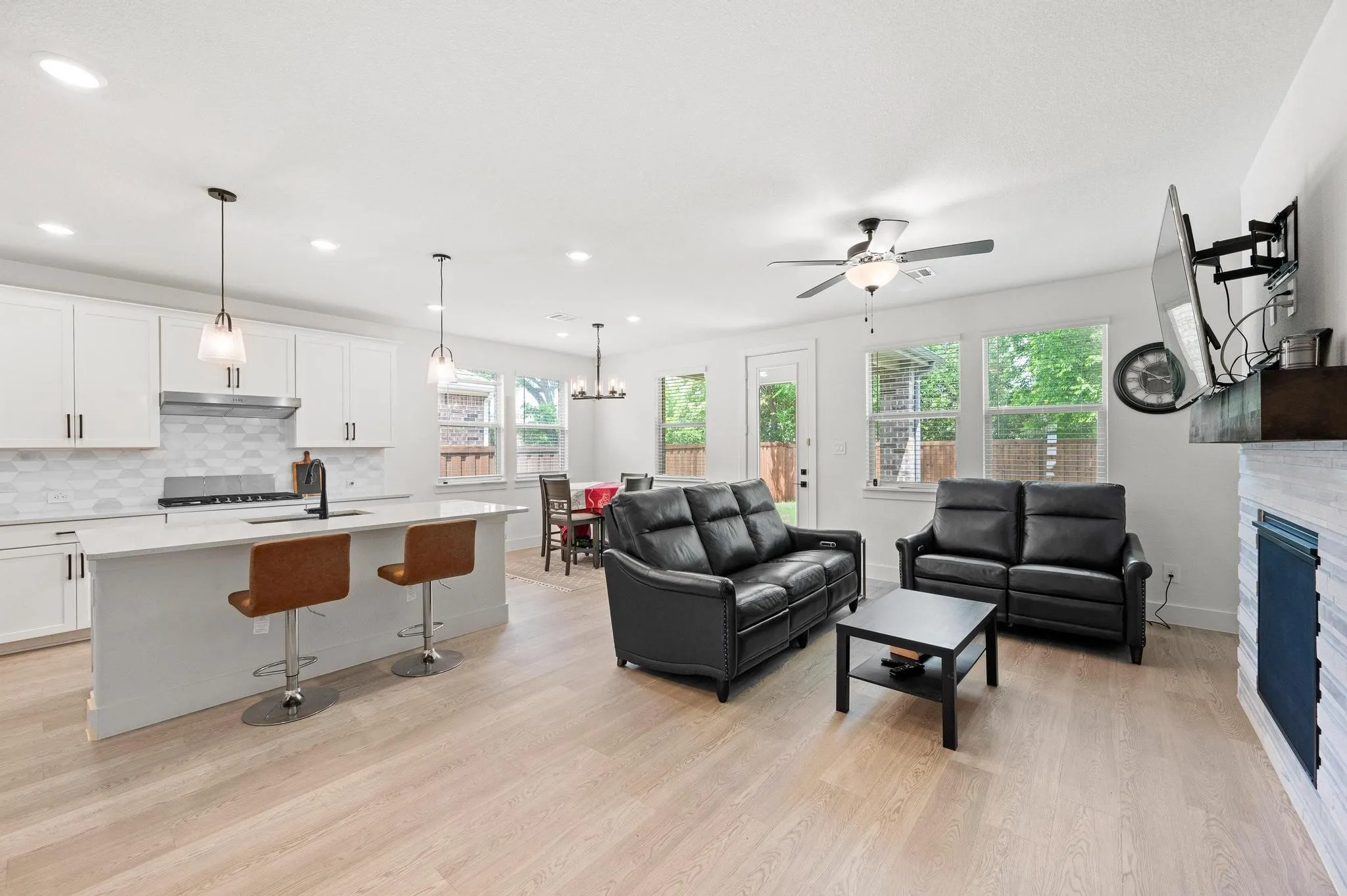 Open-concept living space featuring wood-finish flooring, a kitchen island with pendant lighting, white cabinetry, a tile backsplash, and a ceiling fan