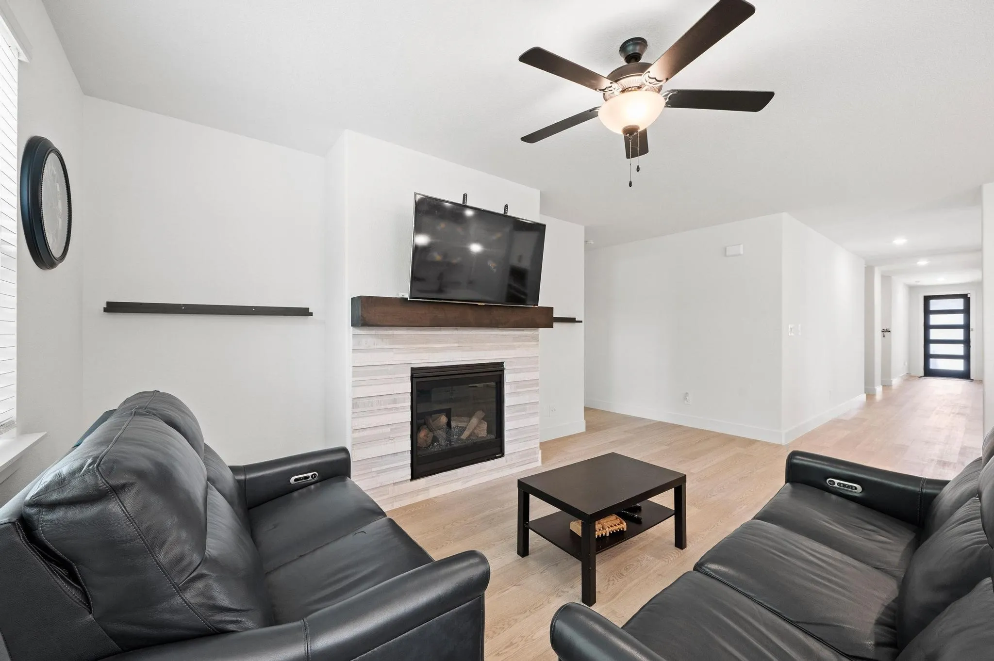 Living area featuring a modern fireplace with a wood-finish mantel, light wood-finish flooring, and a ceiling fan with integrated lighting