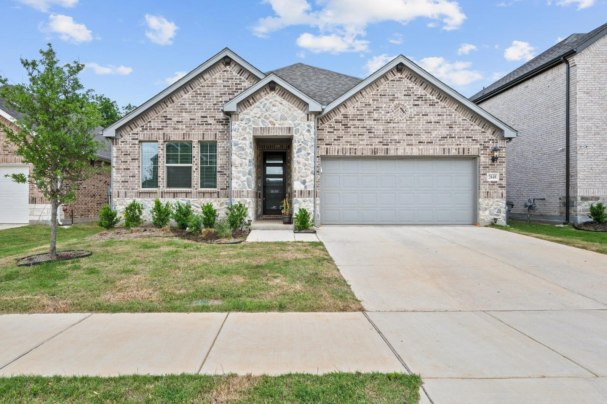Brick and stone exterior with a gabled roofline, concrete driveway, and an attached garage