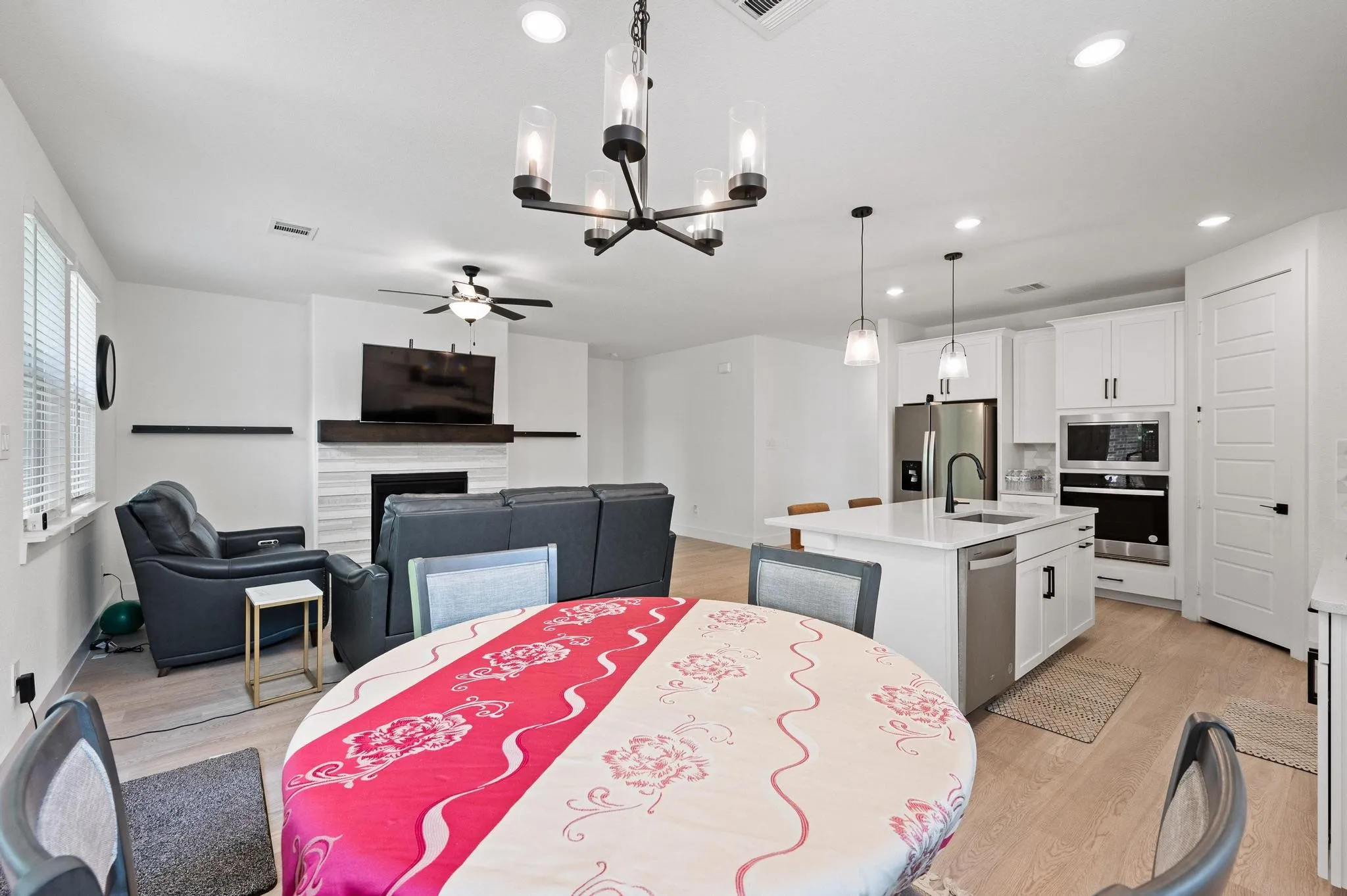 Open-concept living space featuring wood-finish flooring, a white-tiled fireplace with a wood mantle, and a kitchen island with seating