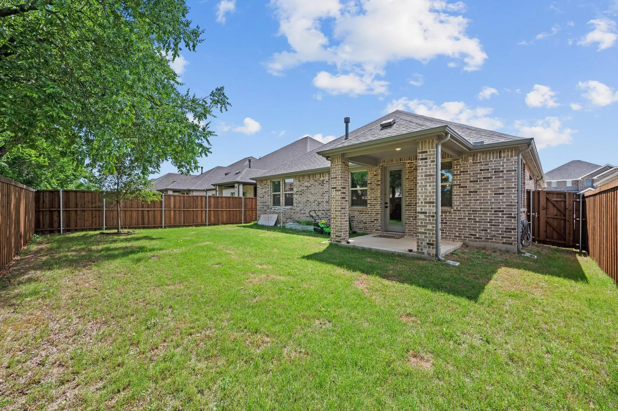 Expansive backyard featuring a manicured lawn, full privacy fencing, and a covered concrete patio
