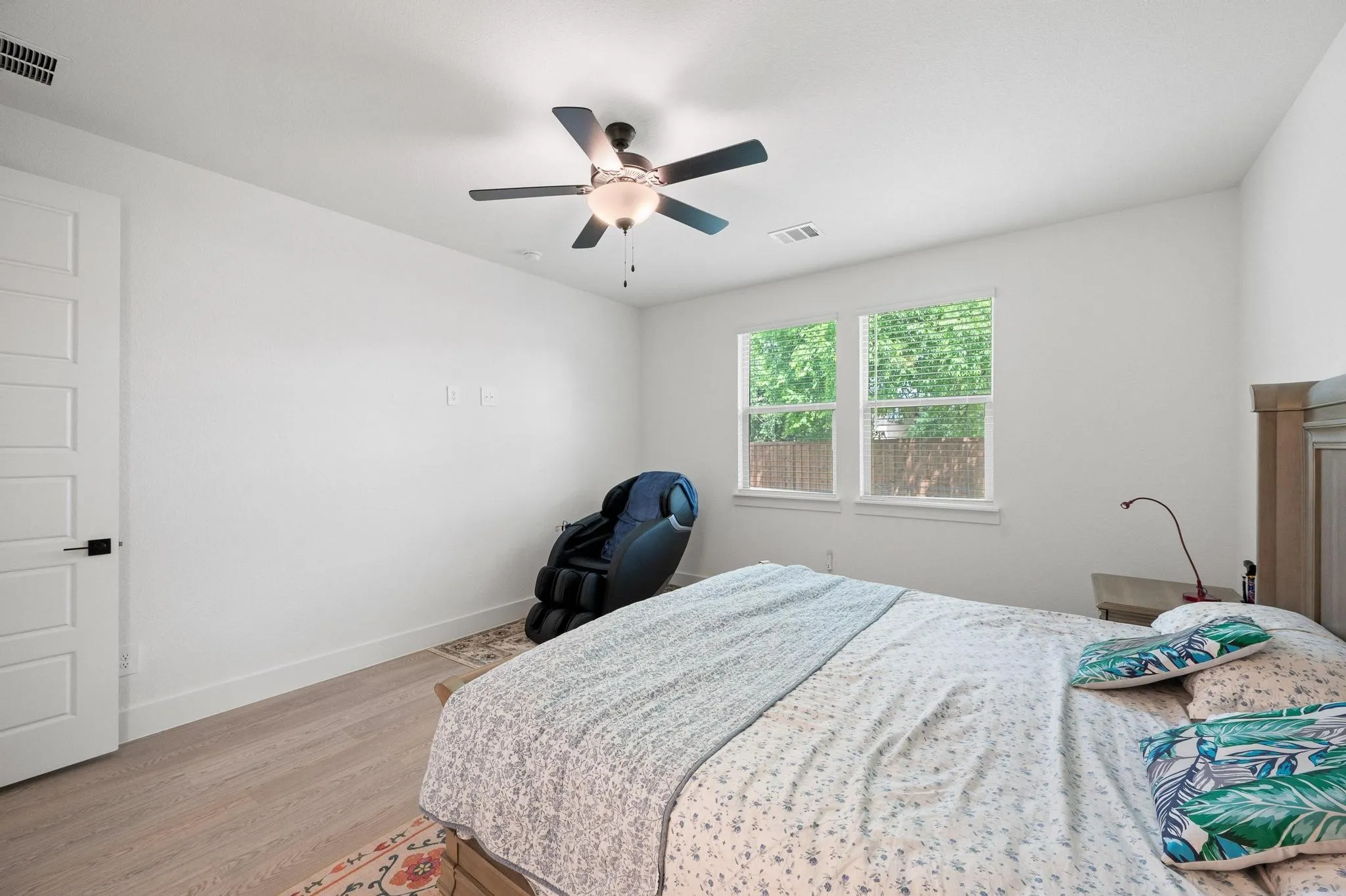 Wood-finish flooring, white paneled door with black hardware, ceiling fan with integrated lighting, and dual windows