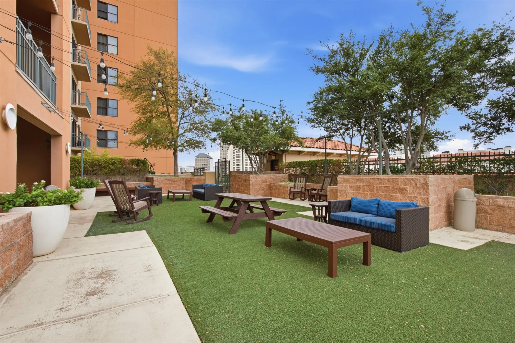 Expansive outdoor terrace featuring artificial turf, string lighting, and stone planter walls
