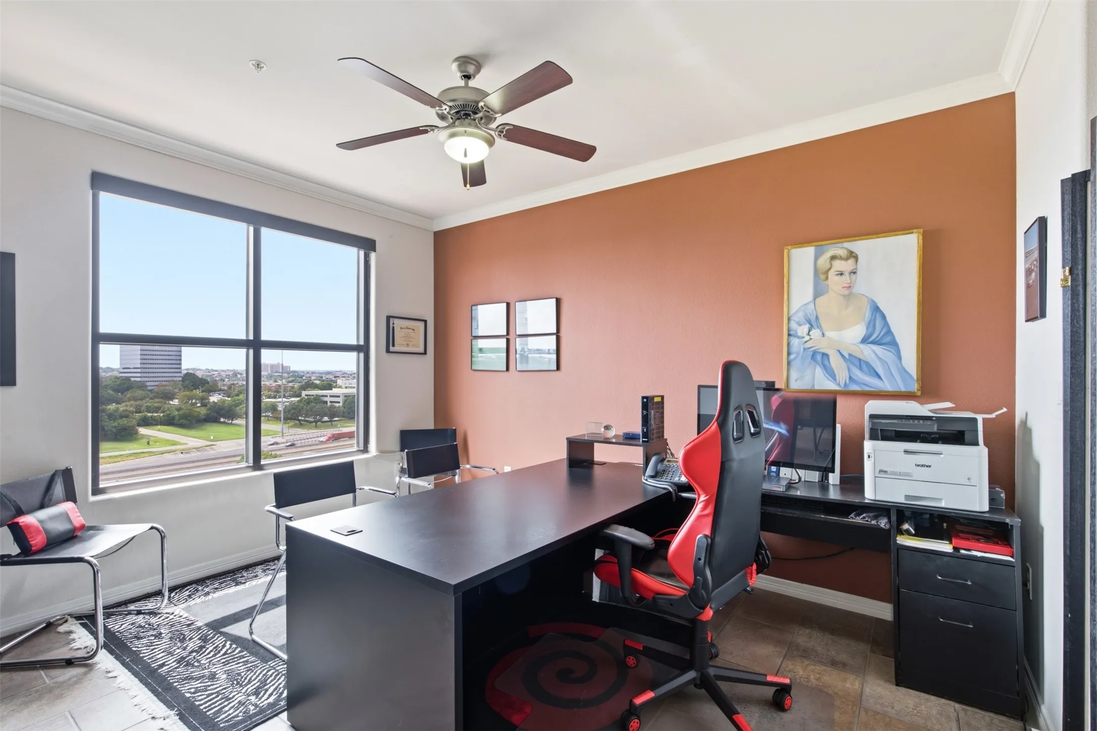 Large windows offering urban scenery, crown molding, a ceiling fan with integrated lighting, wood-finish flooring, and a spacious desk area