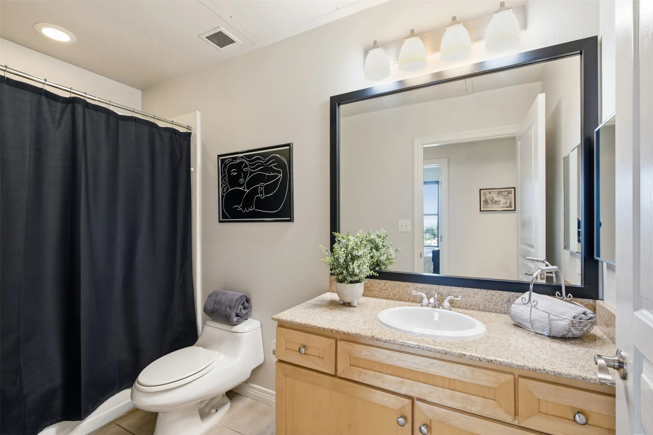 Single vanity with light wood-finish cabinetry, a stone-finish countertop, and an undermount sink